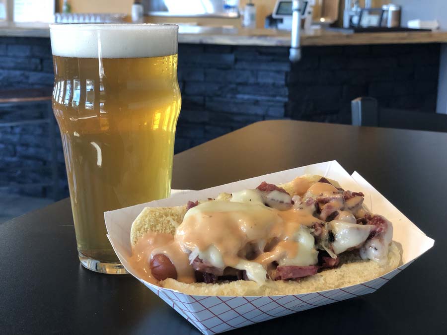 A paper container of food next to a glass of beer on a table.