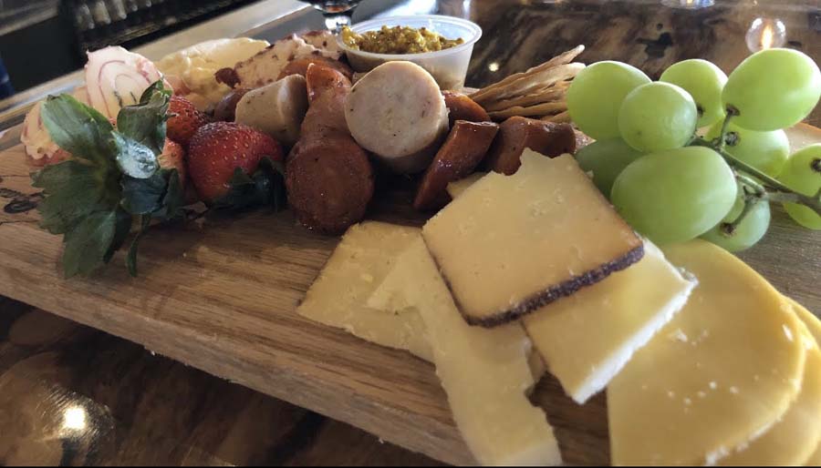 A wooden cutting board topped with sliced cheese , grapes , strawberries and crackers.