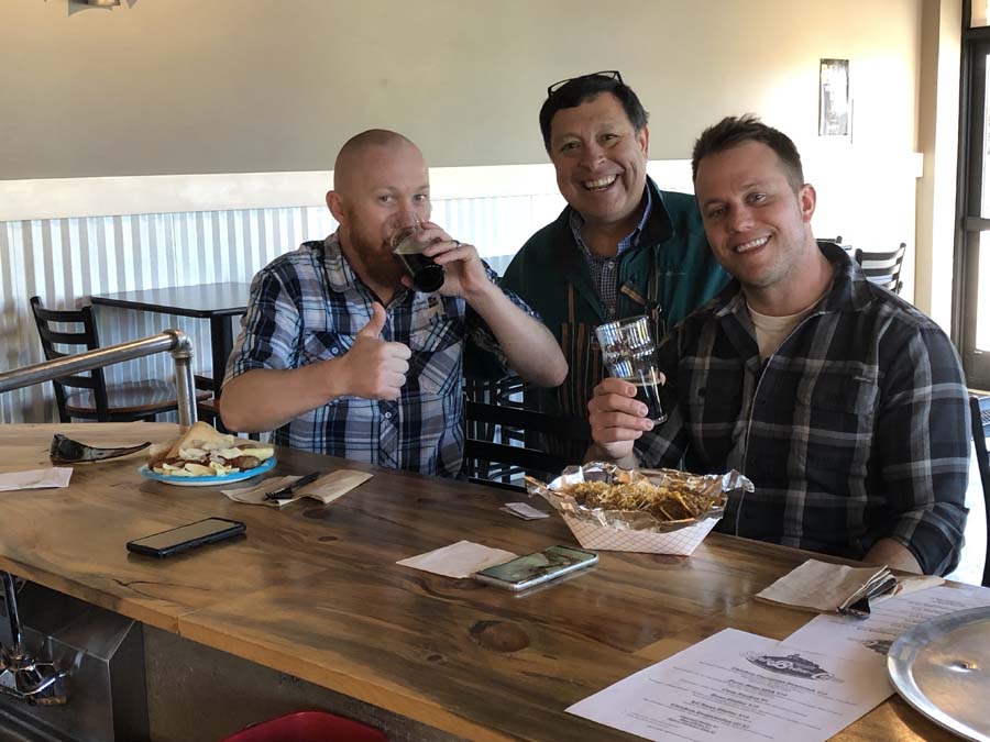 Three men are sitting at a table drinking beer and eating food.