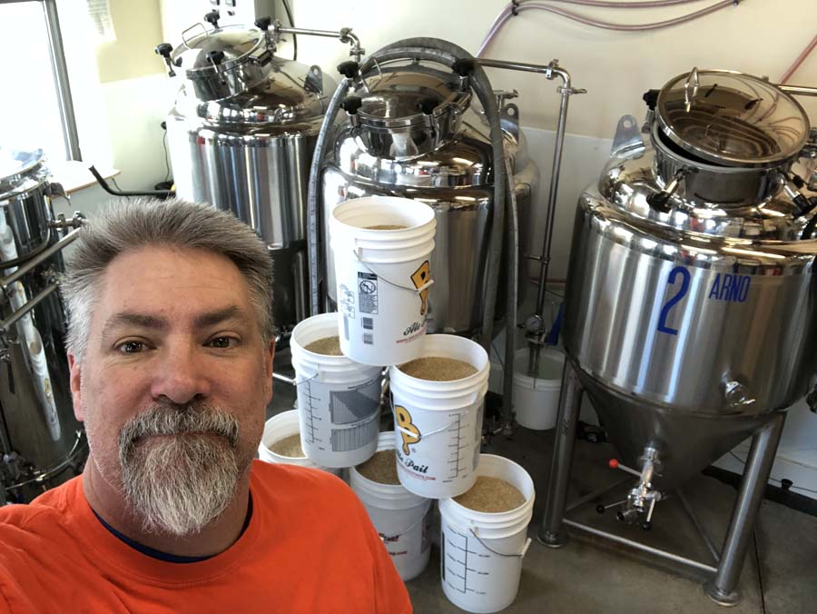 A man is standing in front of a stack of buckets in a brewery.