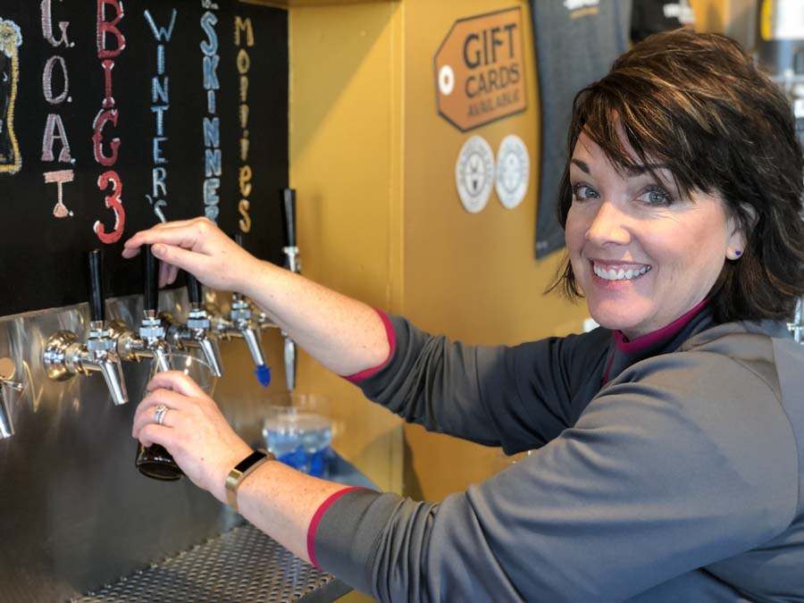 A woman is pouring beer from a tap in front of a sign that says gift cards