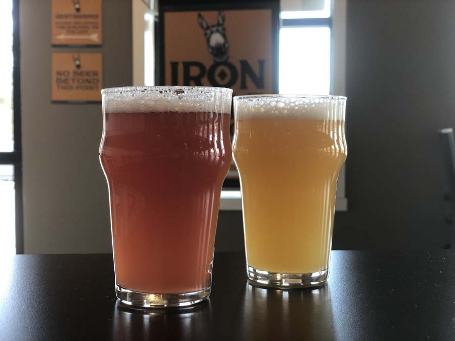 Two glasses of beer are on a table in front of a sign that says iron
