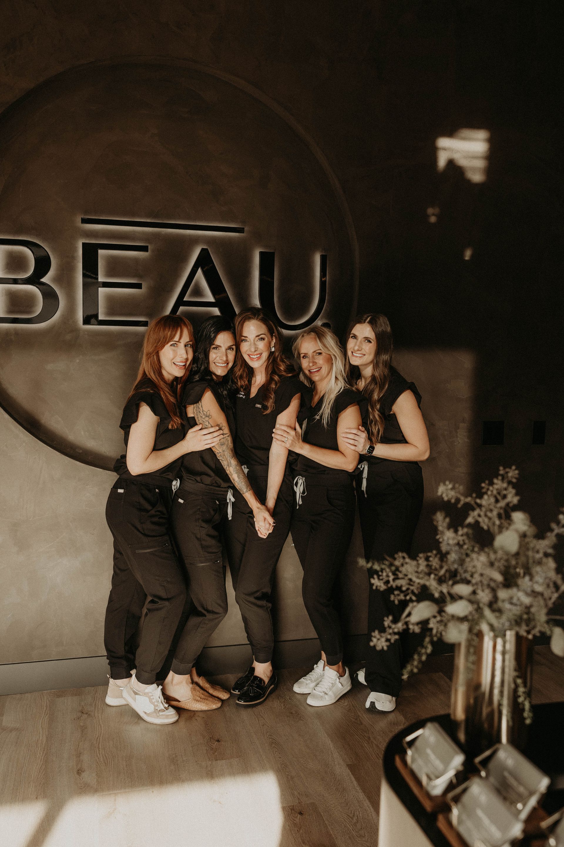 Six women in black scrubs stand in front of a 
