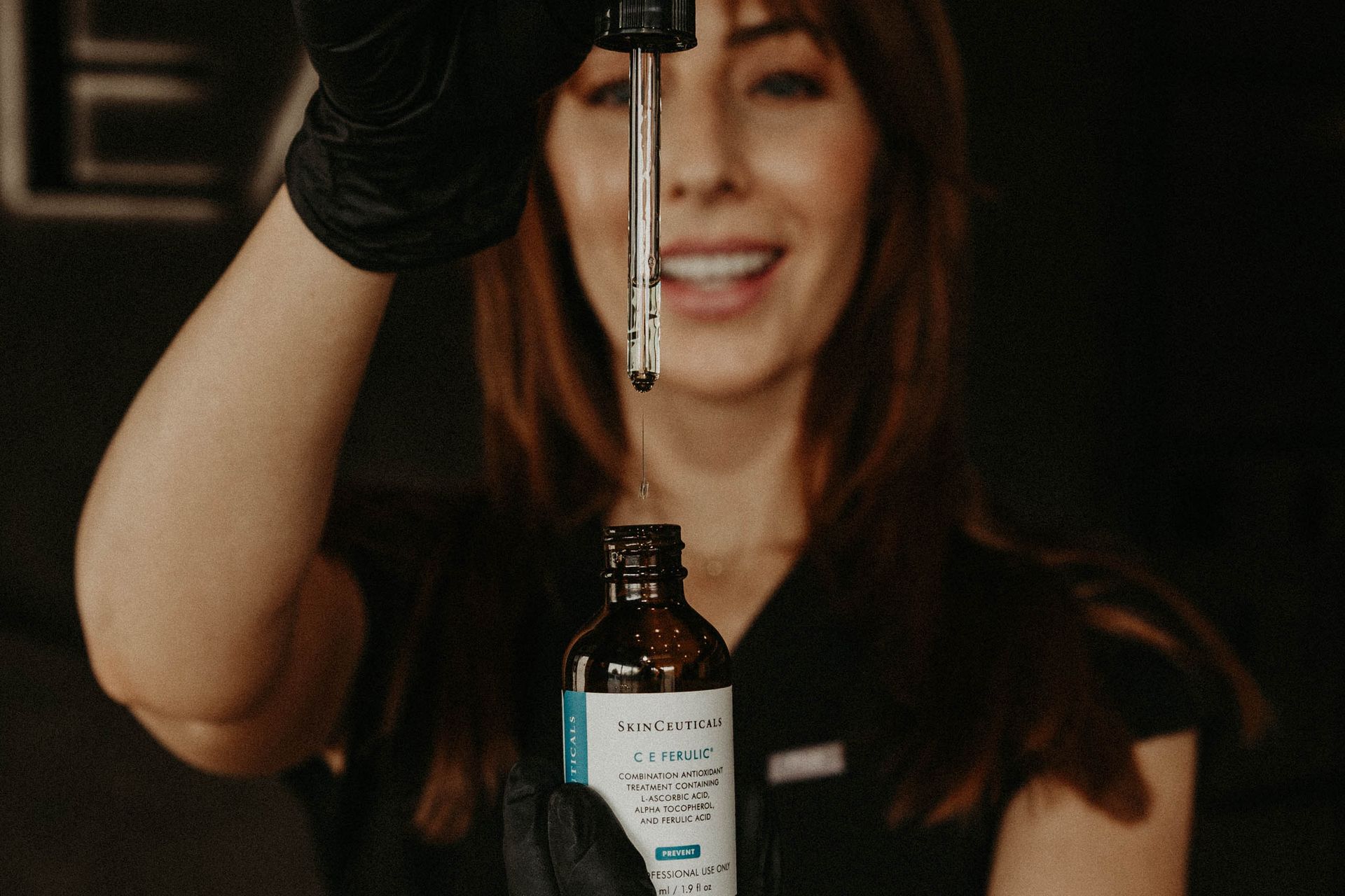 Woman dispensing liquid from dropper bottle. She wears black gloves and smiles.
