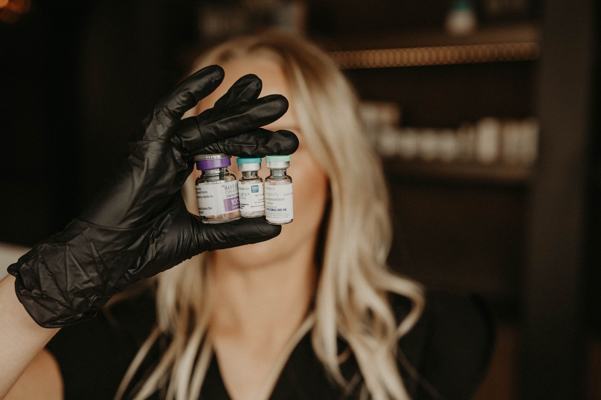 Woman in black gloves holding three small vials.
