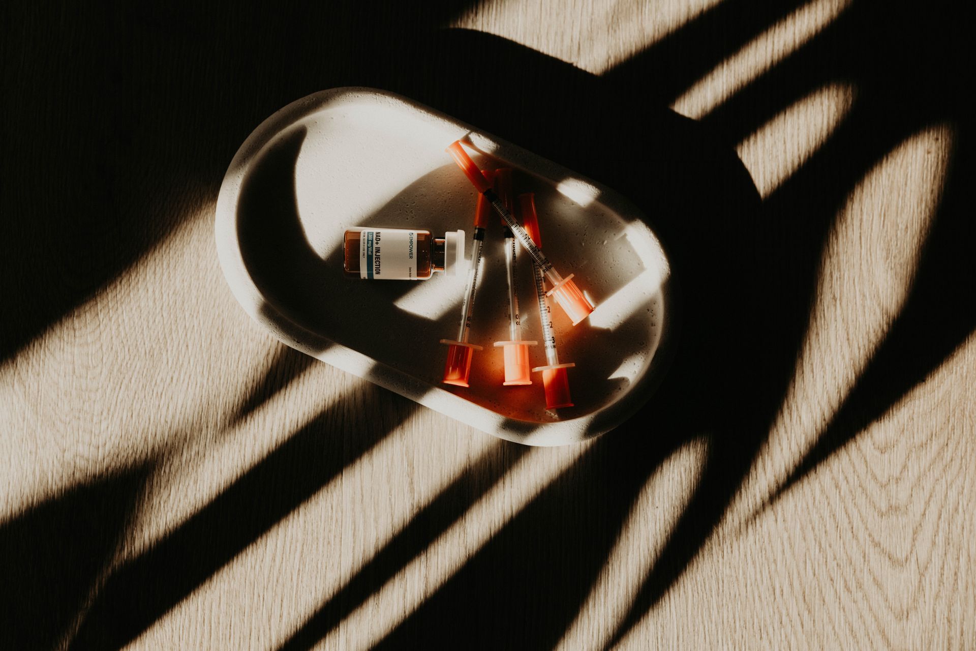 Glass bowl with red candles on a wooden floor, lit by strong window shadows