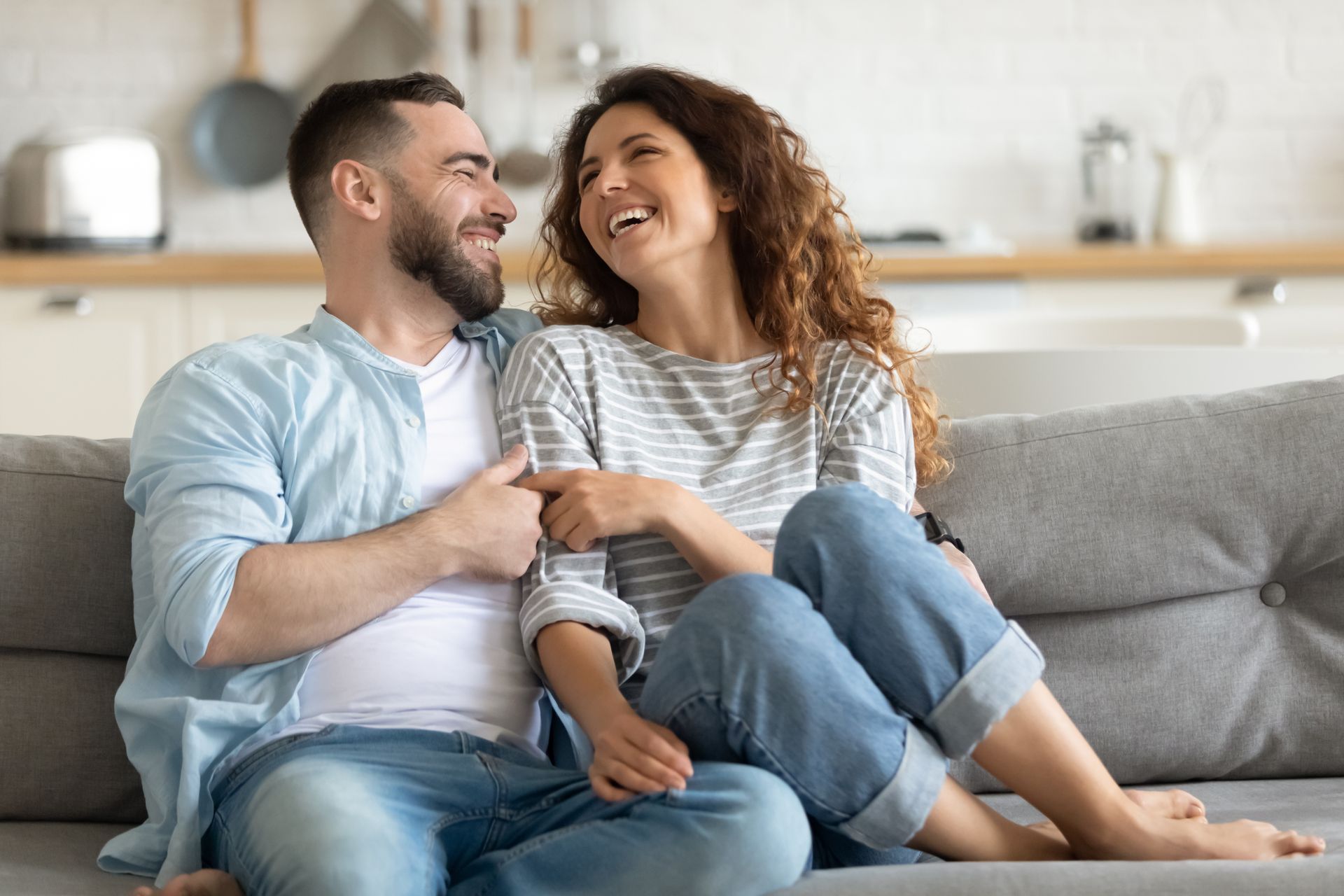 Two people sitting on a couch, smiling and holding hands in a bright living room