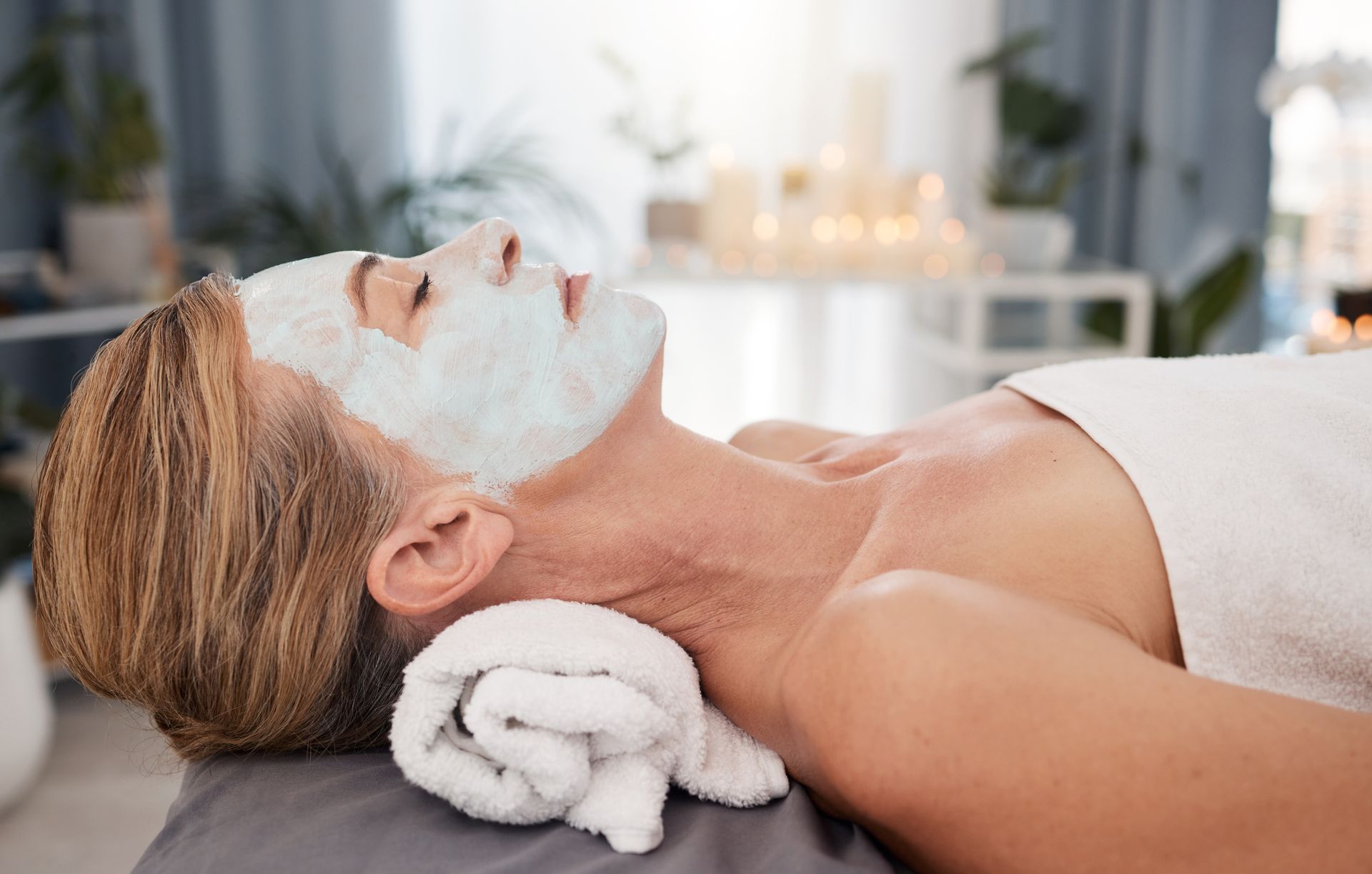 Woman lying on a spa table with a white facial mask and towel under her head