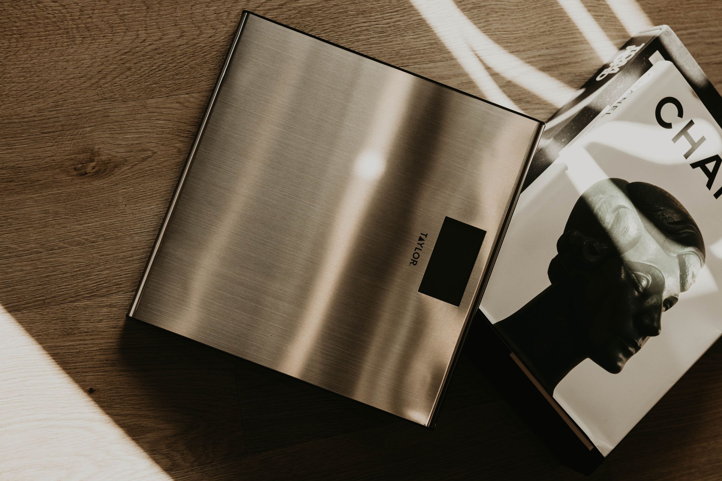 Digital scale and a book on a wooden surface, sunlight casting shadows.