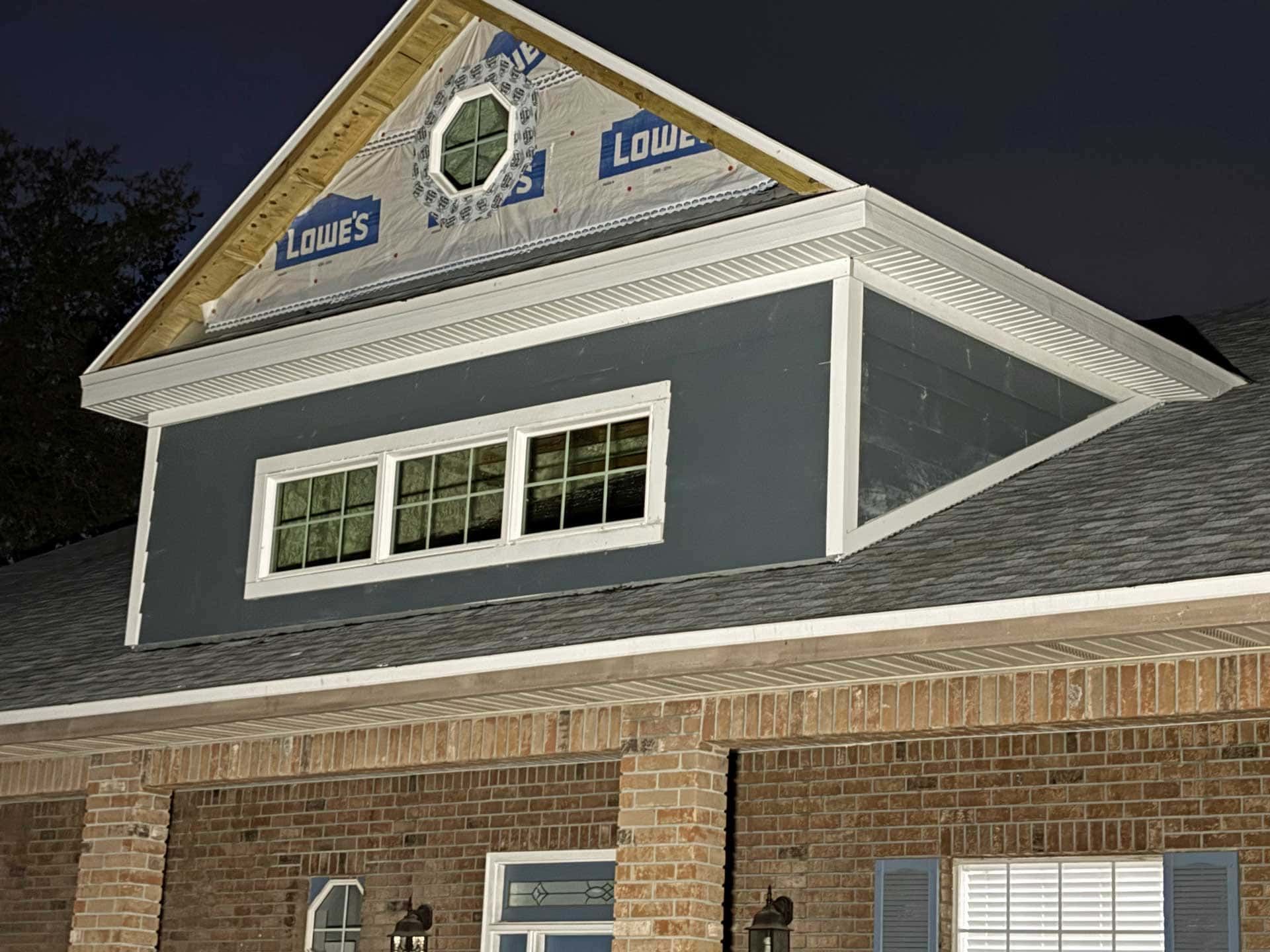 Exterior view of a dark blue dormer with white trim, set atop a brick home with an open attic.