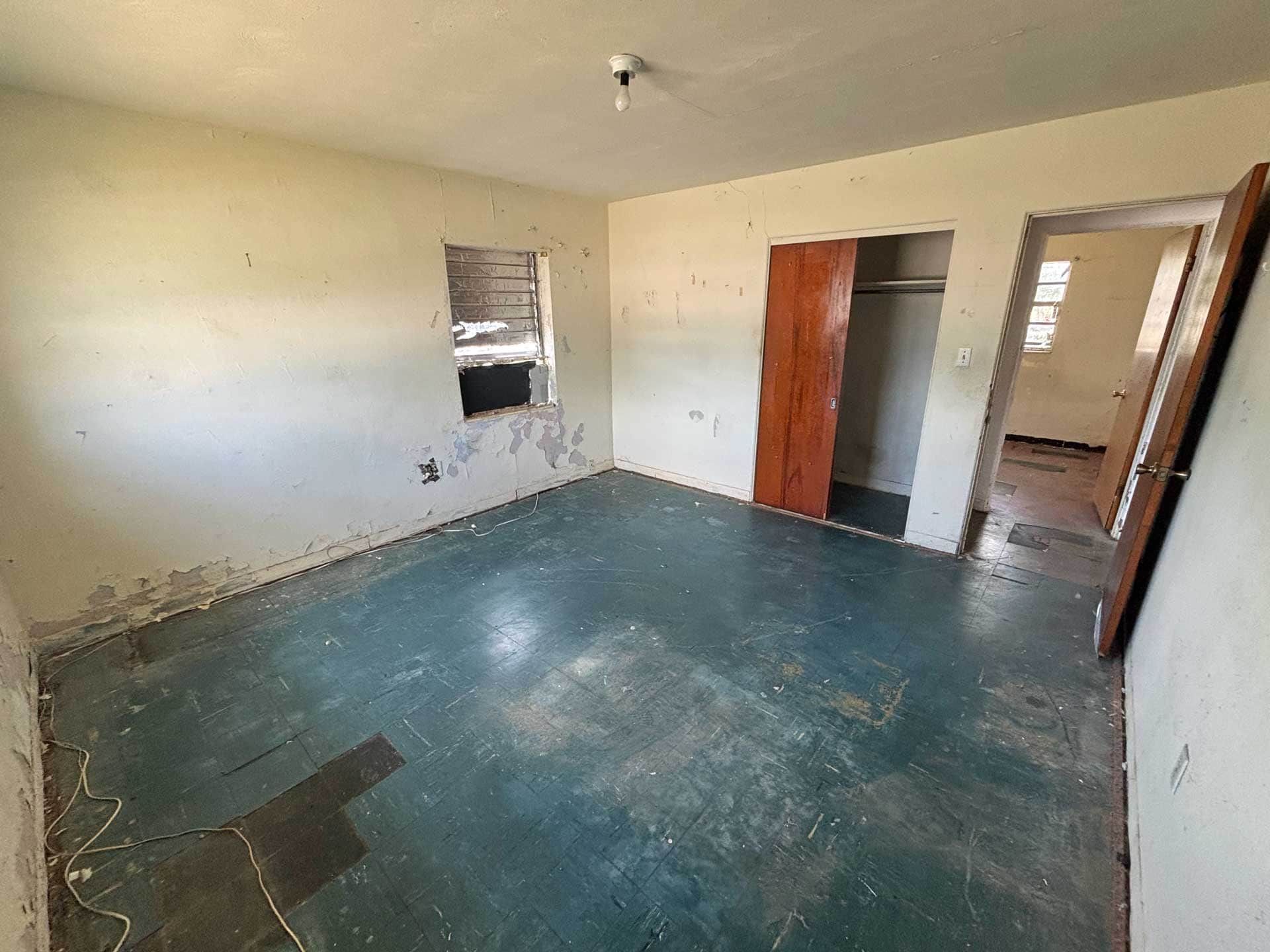 Empty room with peeling paint, teal floor, a closet, and doorway.