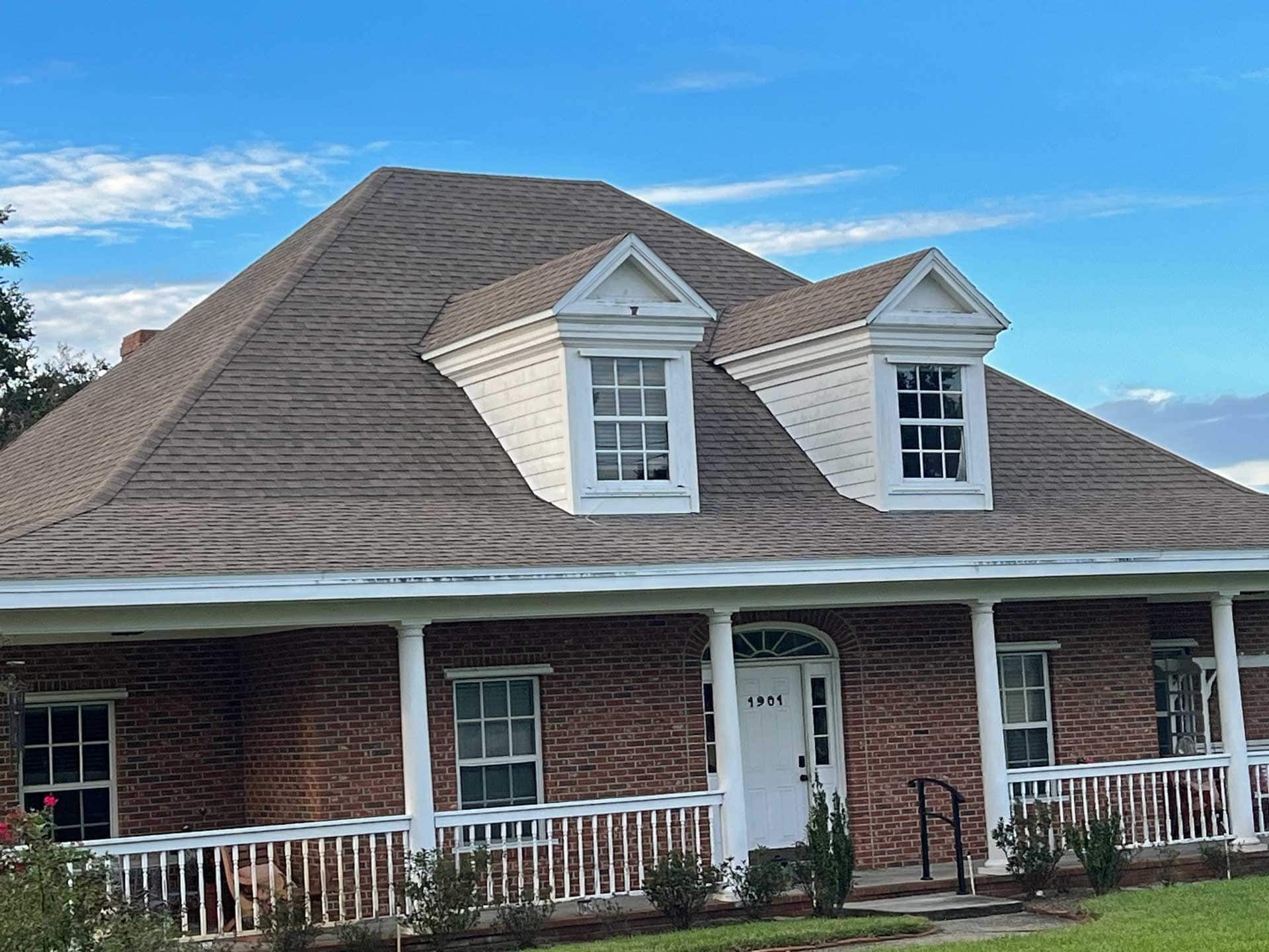 Brick house with brown roof, two dormers, and white porch.