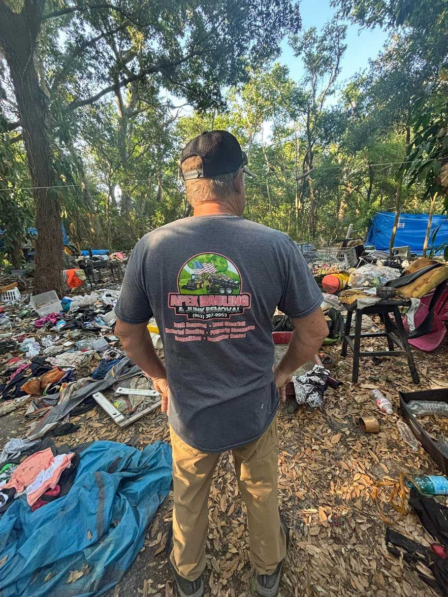 Man in gray shirt stands in a cluttered outdoor area, looking at the debris.