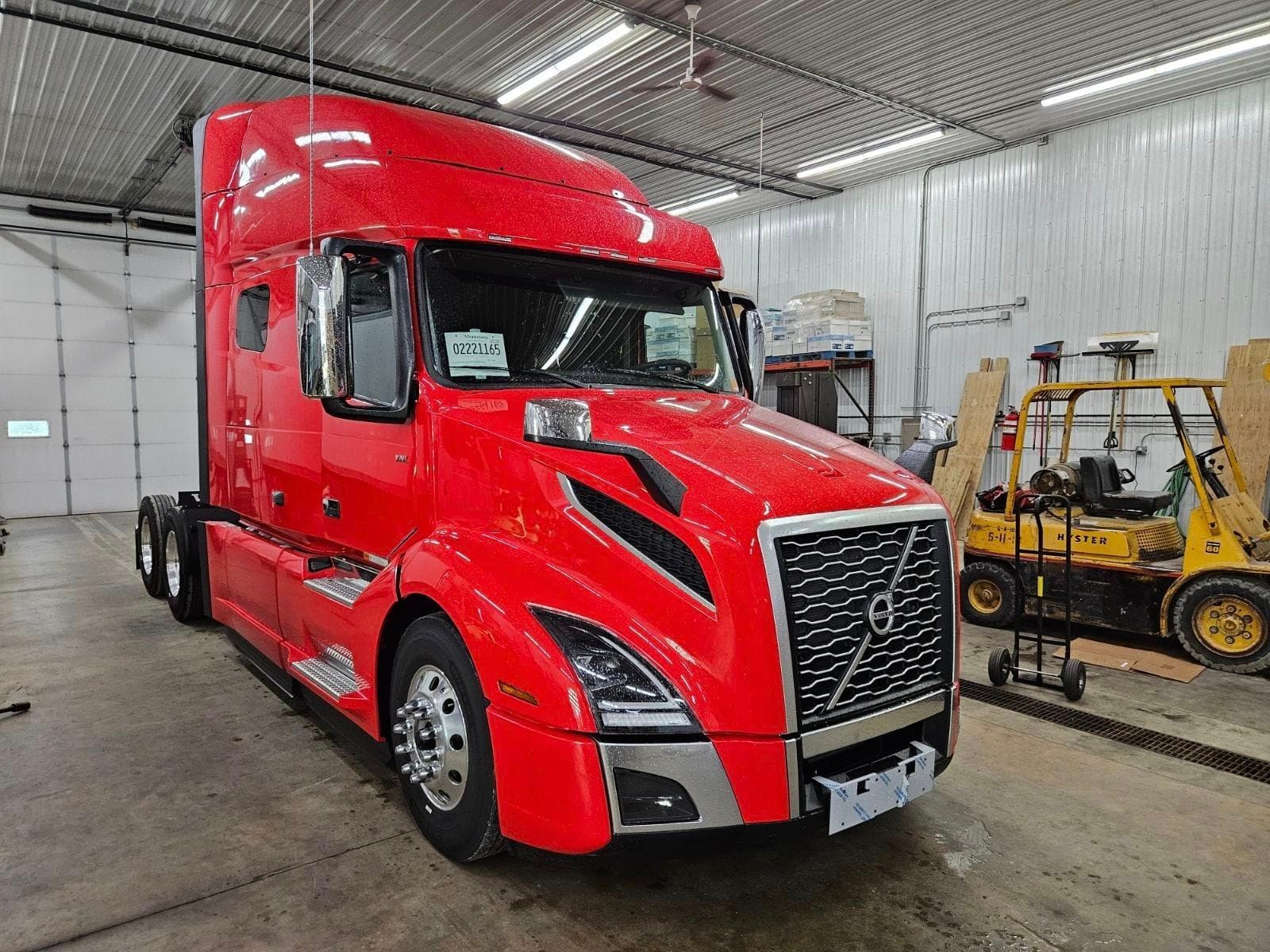 A red semi truck is parked in a garage next to a forklift.