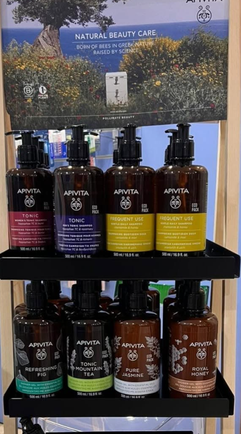 Espositore da scaffale con flaconi di prodotti di bellezza naturali Aviva in vari colori e un cartello promozionale floreale sopra.