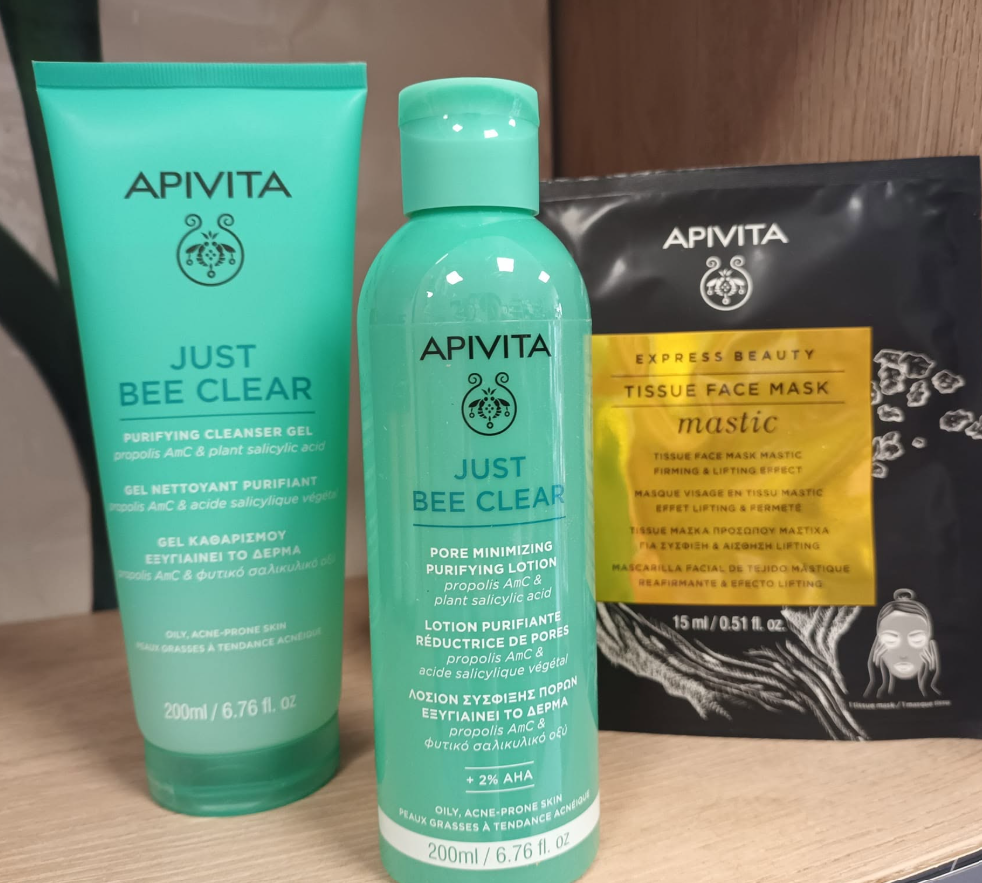 Tre prodotti per la cura della pelle APIVITA Just Bee Clear su una superficie di legno, tra cui due tubetti verde menta e una pochette nera per maschere viso.