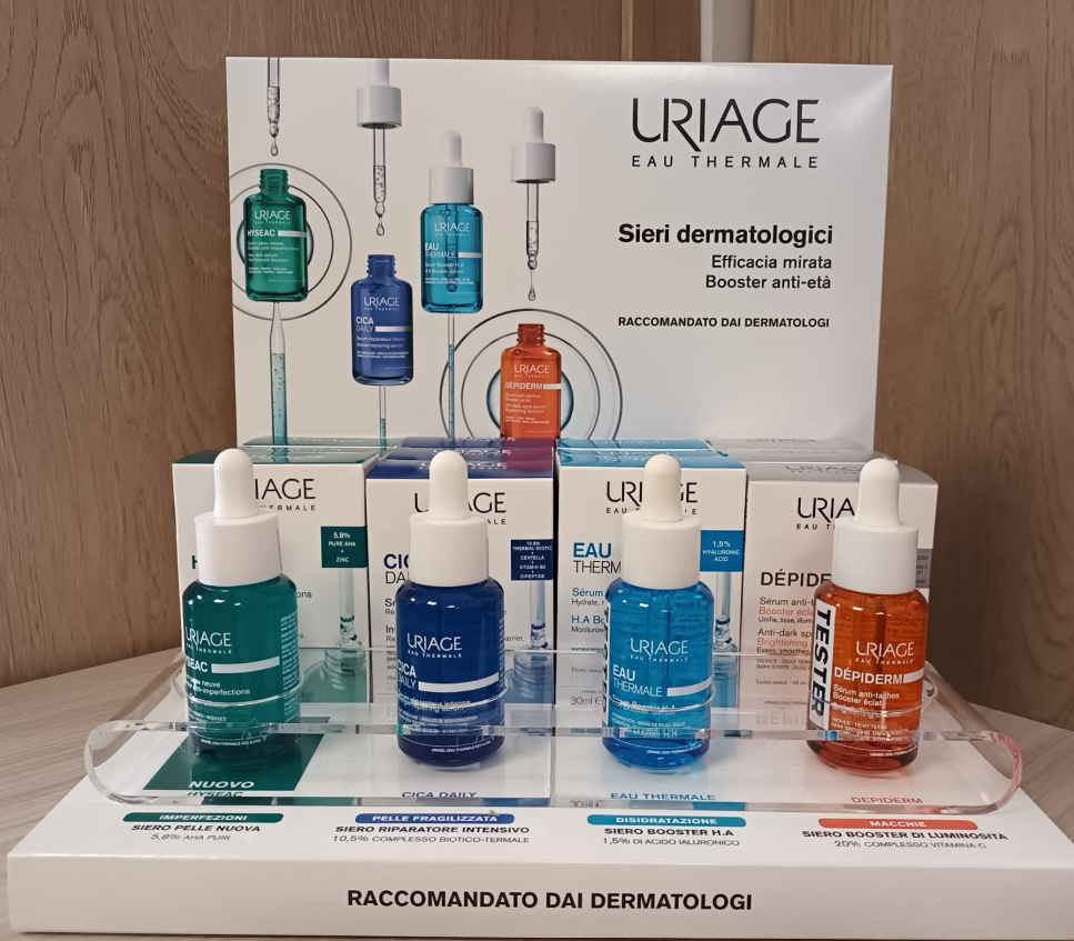 Espositore per prodotti per la cura della pelle URIAGE con flaconi colorati di detergente viso su uno scaffale e un'etichetta del prodotto alle loro spalle.