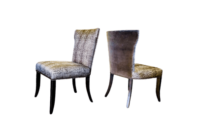 Two upholstered dining chairs, leopard print pattern, dark legs, against a white background.