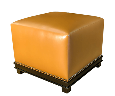 Square, tan leather ottoman on a dark, studded base.