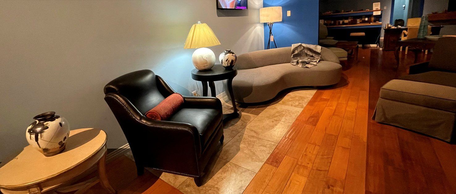 Living room with leather chair, curved sofa, and decorative objects. Warm-toned wood floors, blue and grey walls.