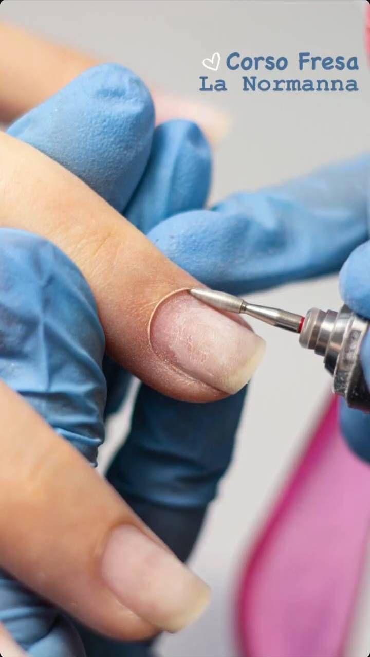 Dito di una persona preparato per la manicure con un trapano per unghie da qualcuno che indossa guanti blu.