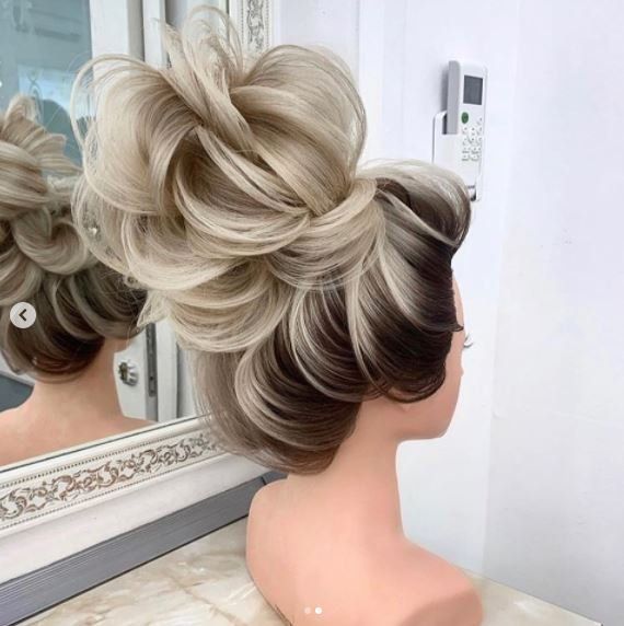 Manichino con elaborata acconciatura raccolta: mèches bionde e castane, riccioli e chignon elaborato.