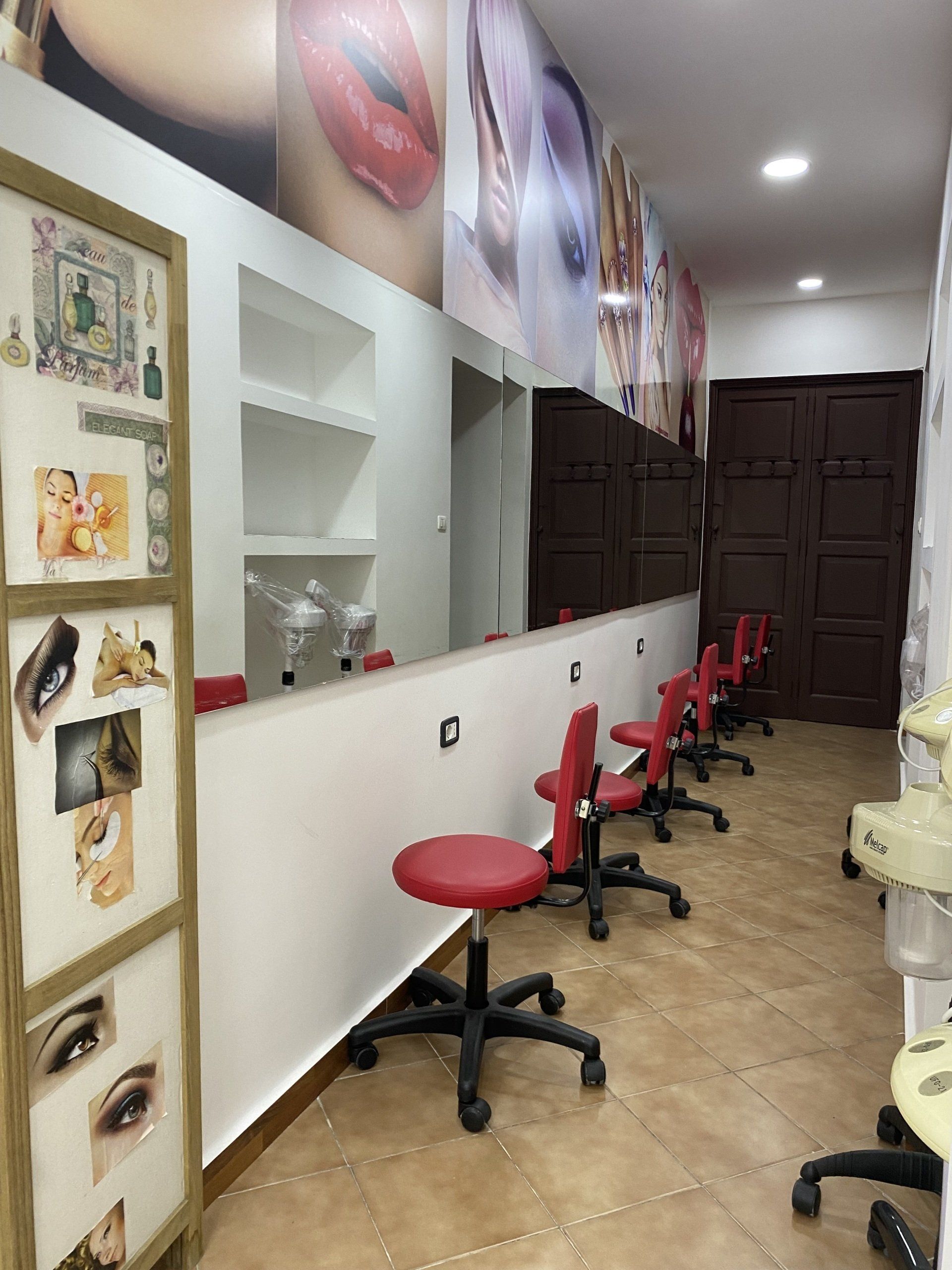 Interno di un salone per unghie con sedie rosse, un lungo specchio e opere d'arte cosmetica alle pareti.