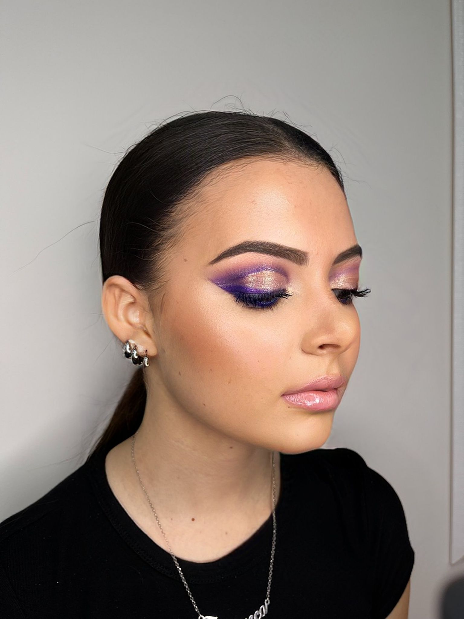 Donna con elaborato trucco occhi viola e rosa, guance illuminate e labbra lucide.
