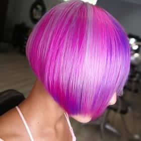 Una persona con un taglio di capelli corto, colorato, rosa e viola.