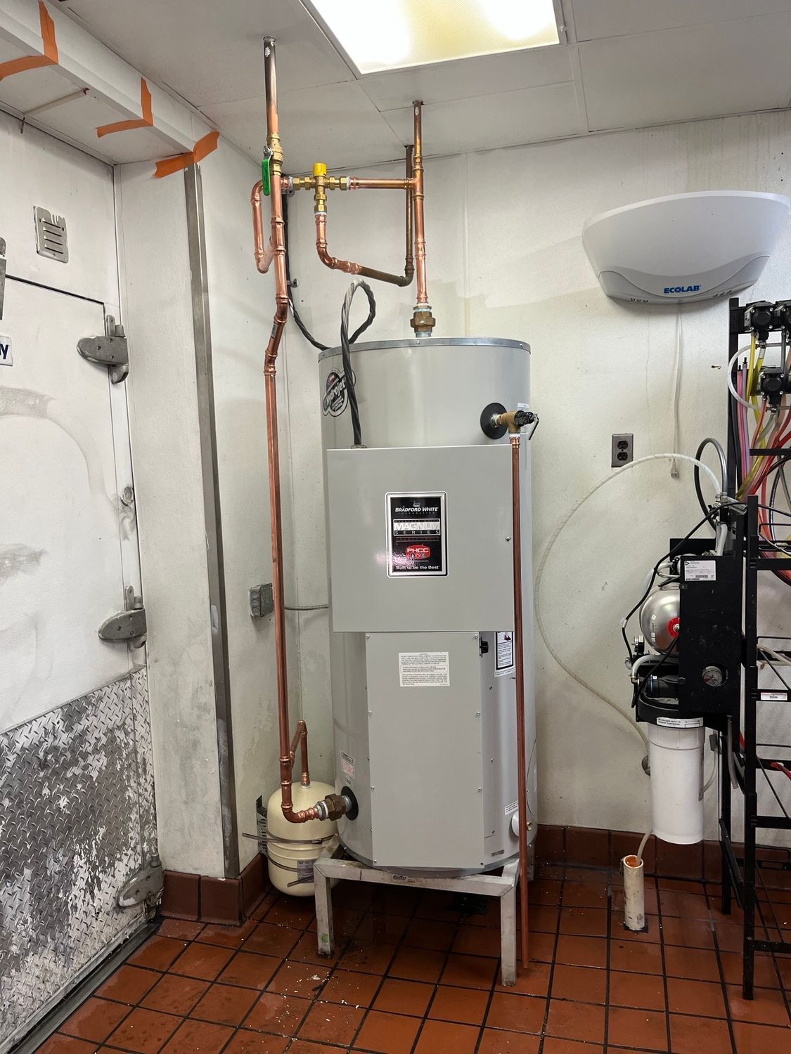 Boiler room with a large white water heater, copper pipes, and tiled floor in a utility space