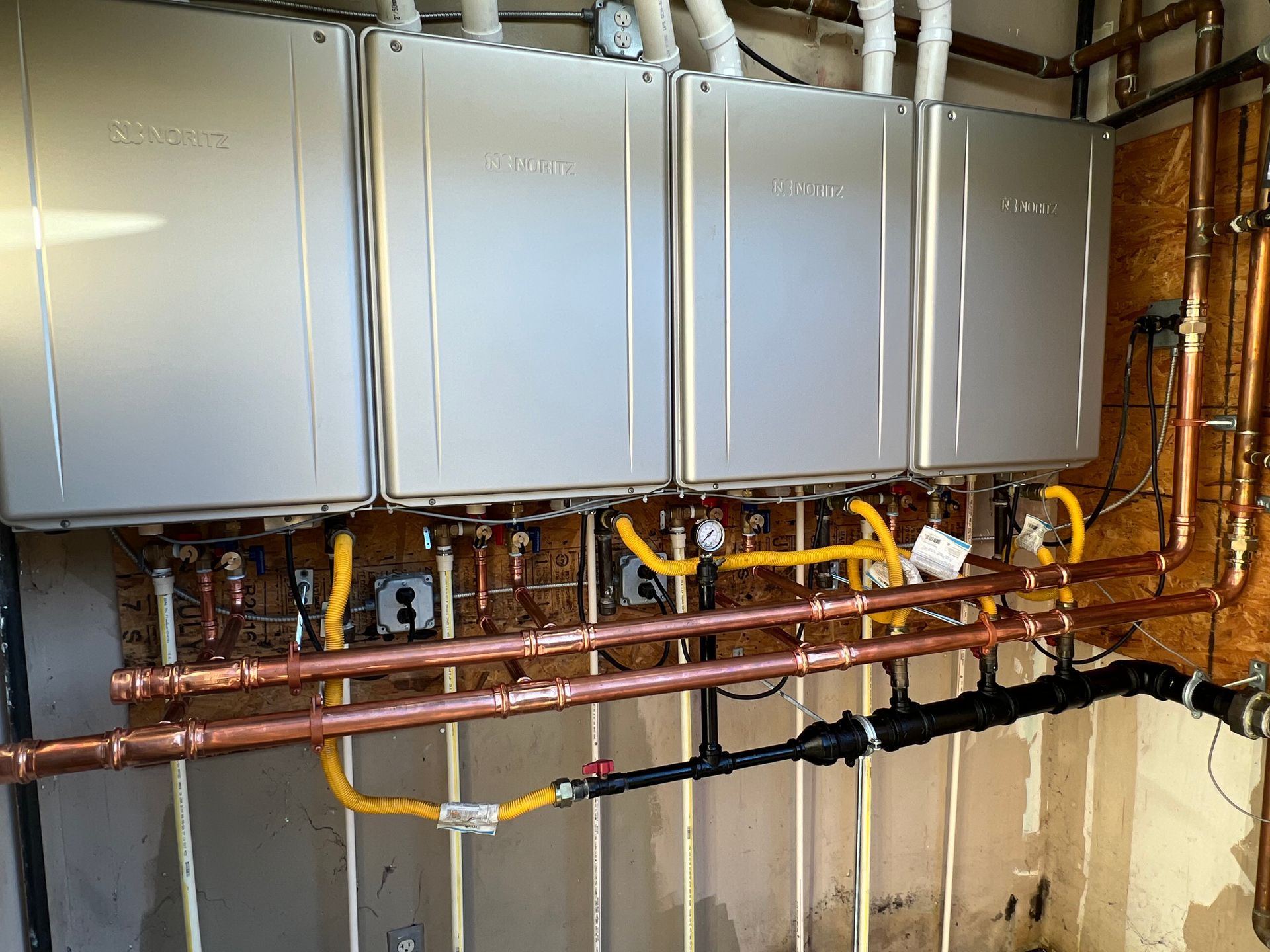 Wall-mounted metal boiler units with exposed copper and yellow gas piping in a utility room