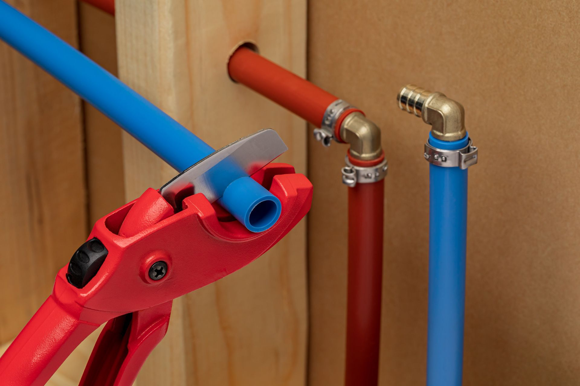 Red pipe cutter cutting a blue pipe among red and blue plumbing pipes