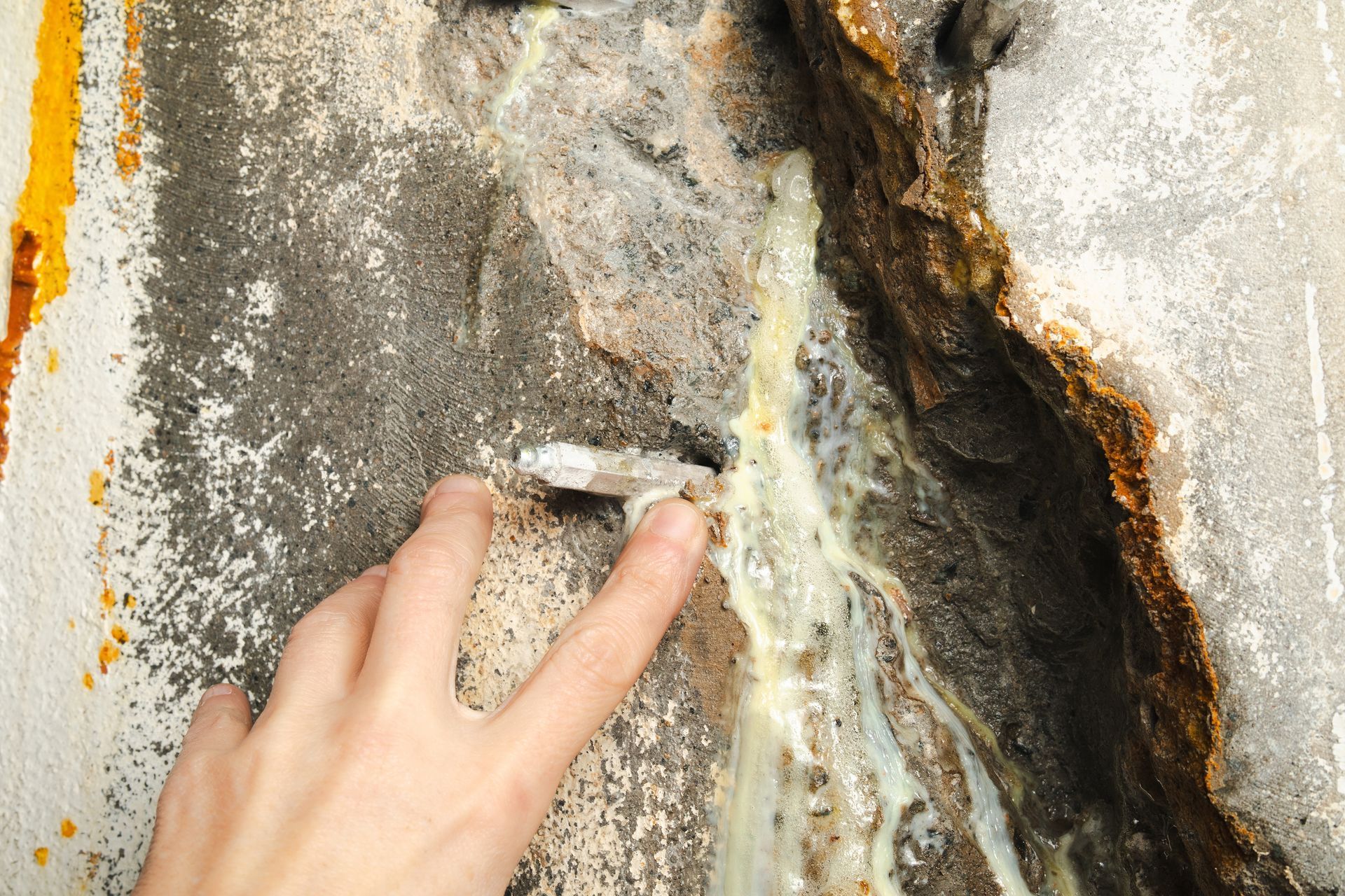 Slab Leak Detection - Hand touching a cracked, weathered concrete wall with peeling paint and exposed rust-stained damage - Savannah, GA