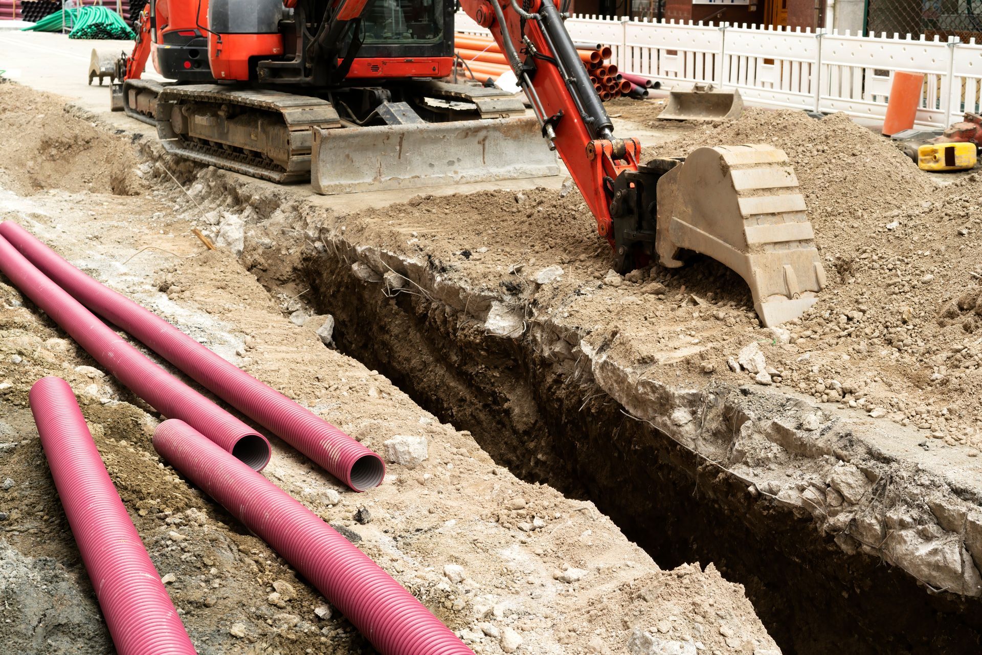 Drain Cleaning & Clog Removal - Excavator digging a trench beside pink utility pipes at a construction site - Savannah, GA