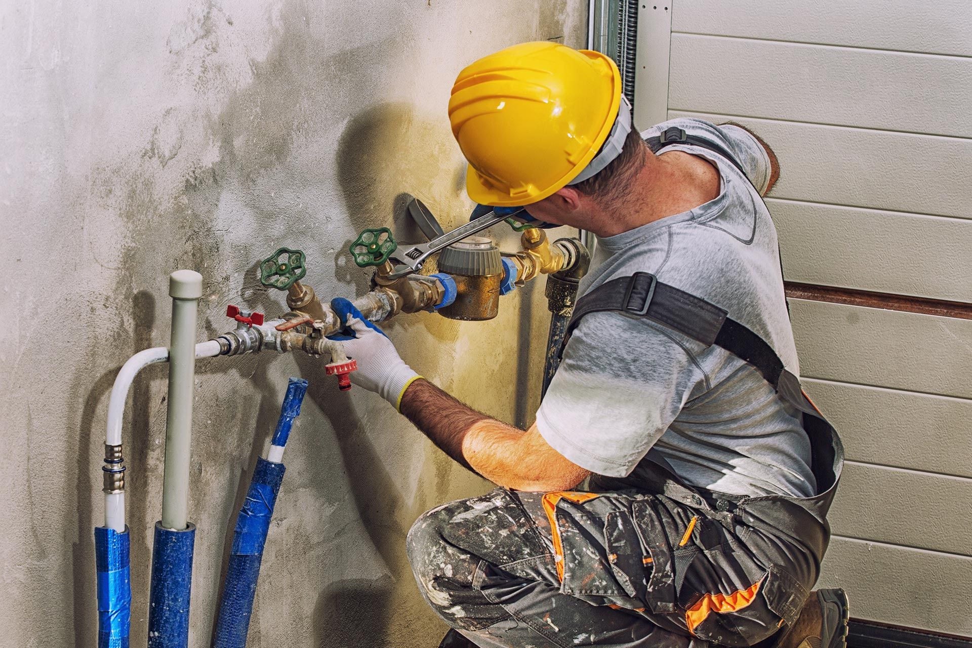 Worker in a yellow hard hat repairs wall plumbing with tools and hoses in a utility area Worker in a yellow hard hat repairs wall plumbing with tools and hoses in a utility area