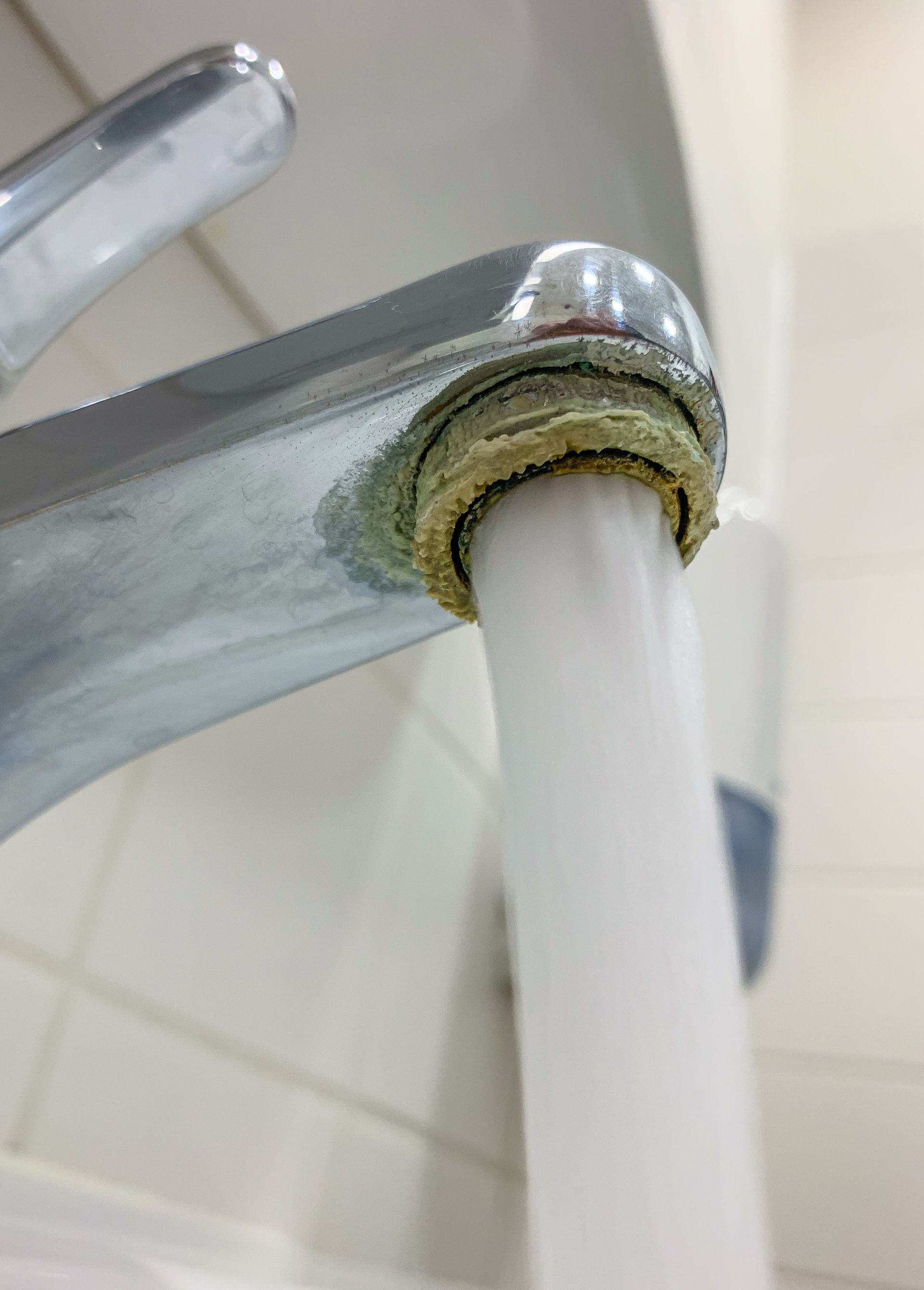 Hard water limescale buildup on a chrome faucet spout with running water.