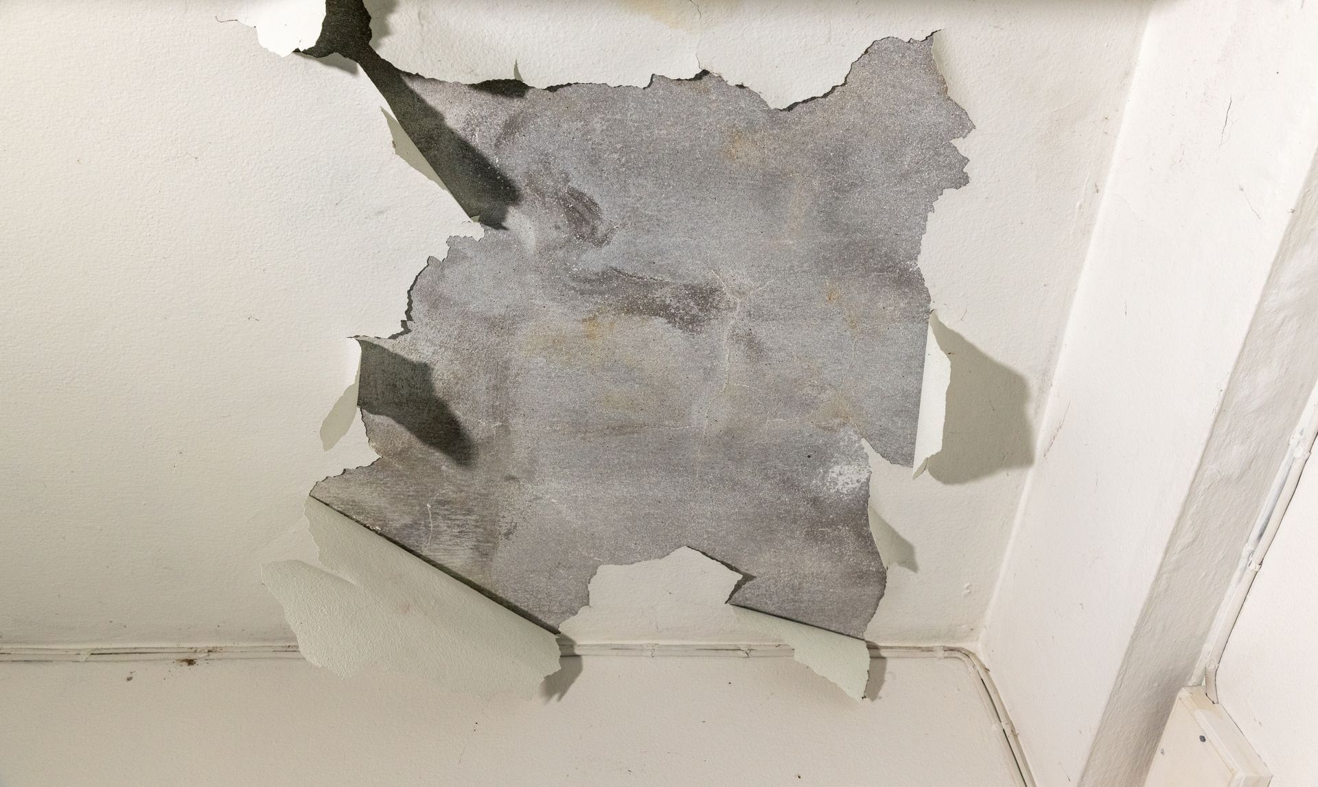Slab Leak Needs Repair - Damaged ceiling with a large gray patch of peeling plaster above a white wall corner - Savannah, GA