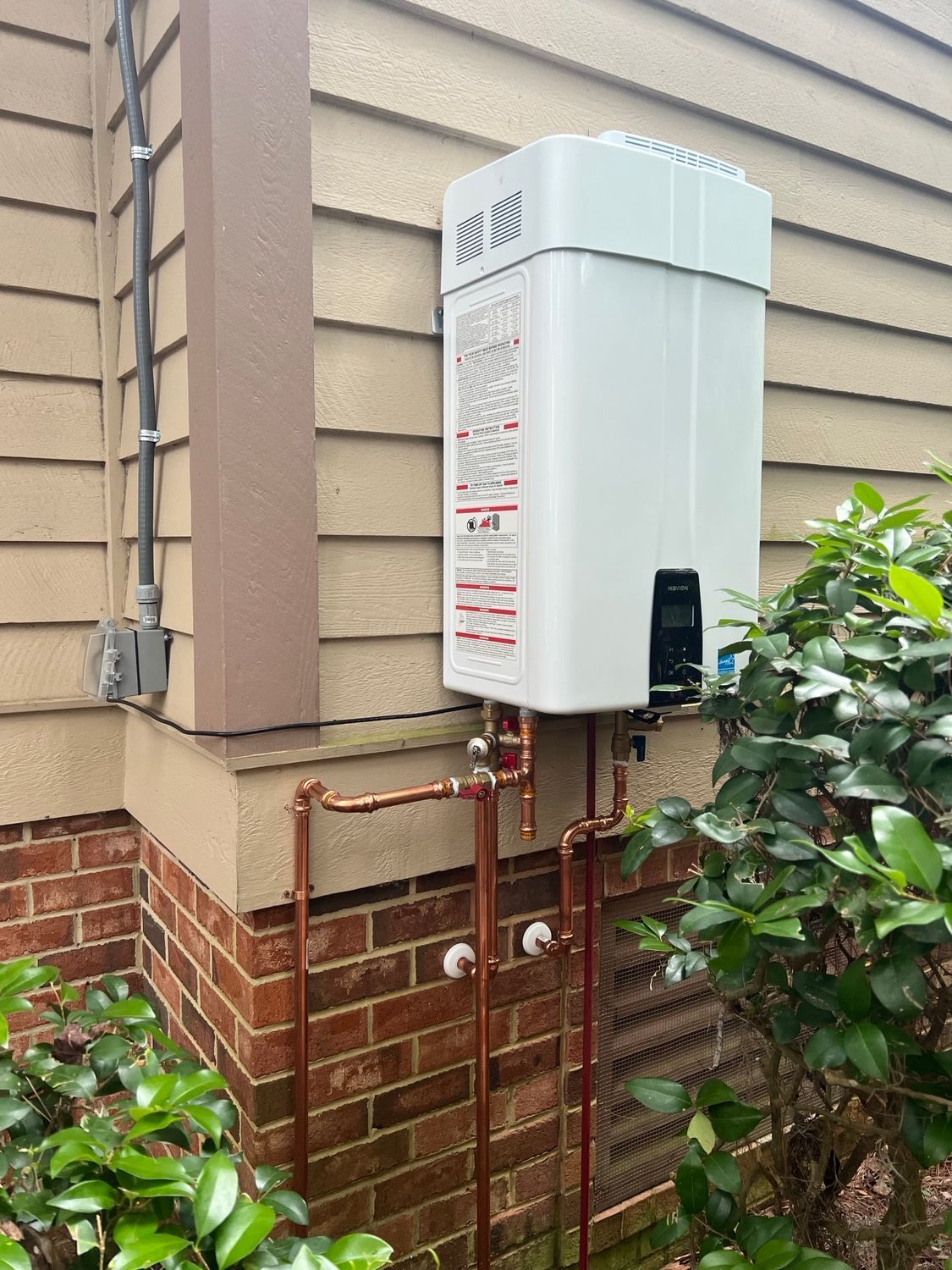 Hand adjusting a wall-mounted gas water heater with exposed pipes and valves.