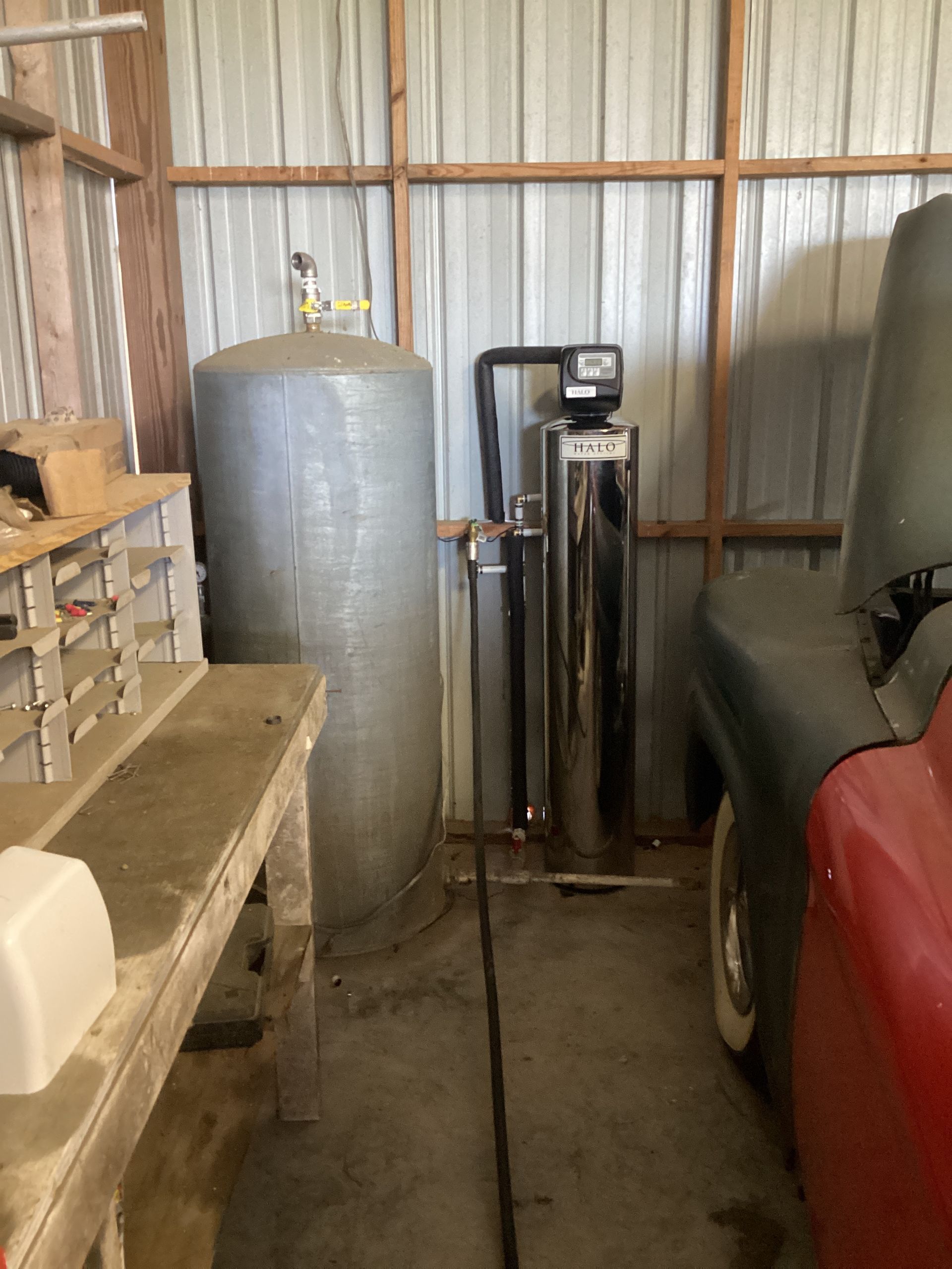 Garage with water softener tank and control unit beside a red vehicle in a metal-walled shed