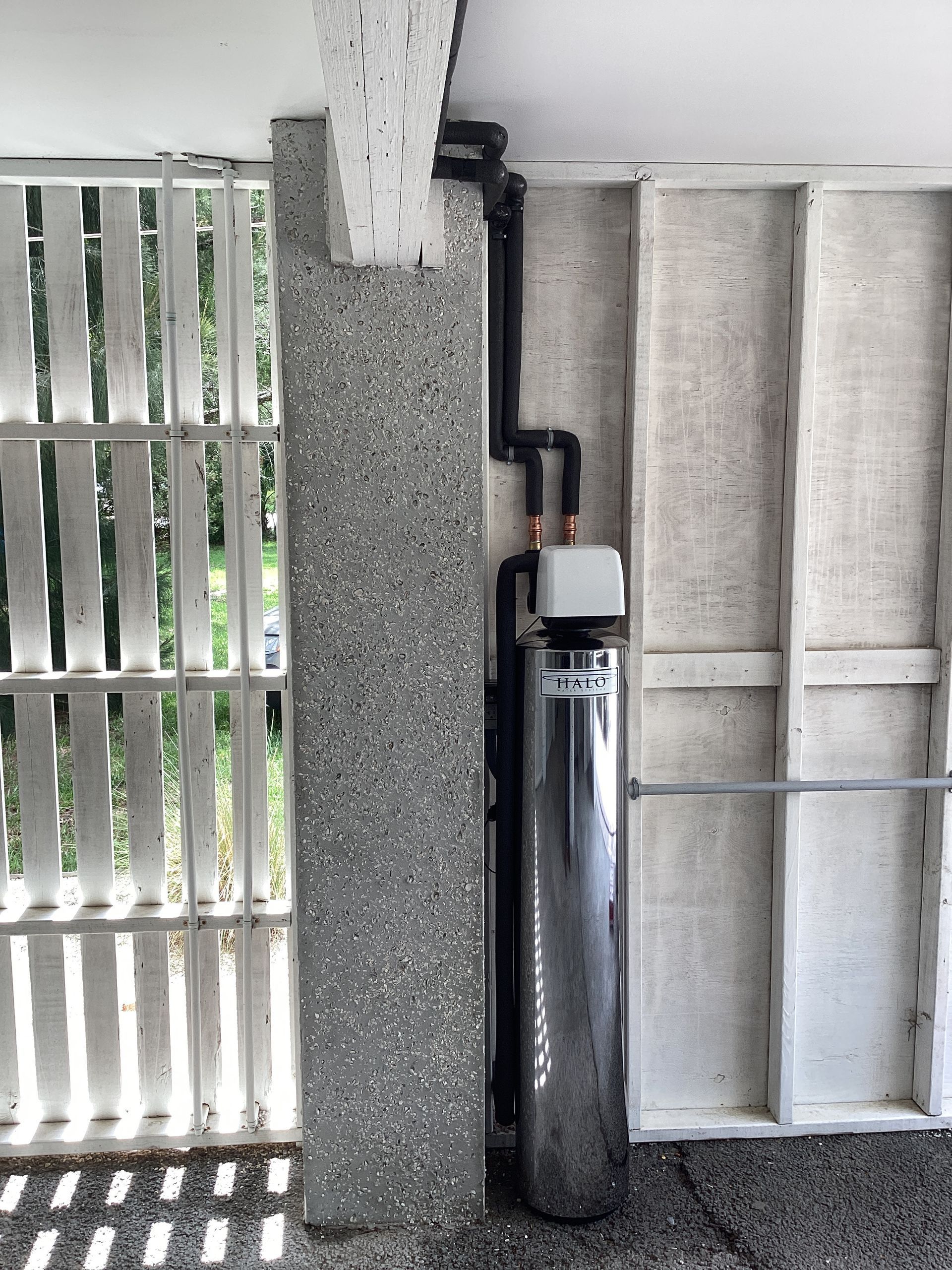 Black utility cylinder mounted beside a speckled wall and louvered window under a covered porch