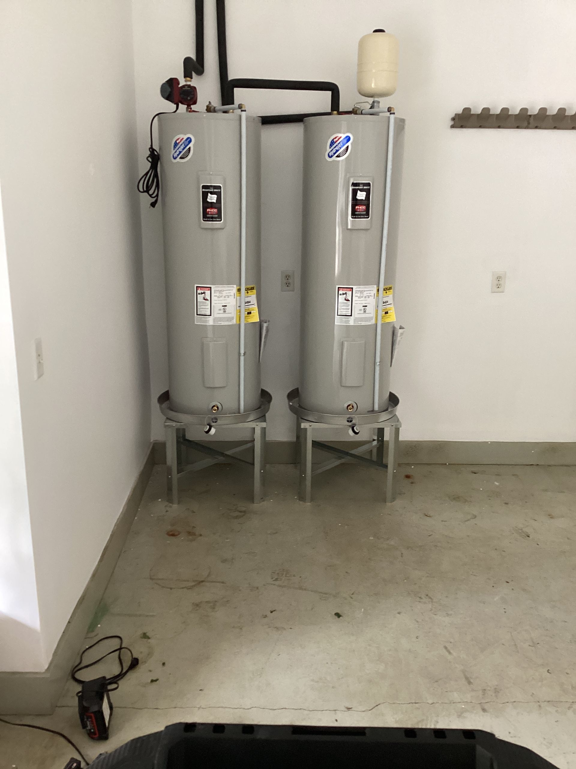 Two gray industrial tanks in a bare utility room with concrete floor and white walls