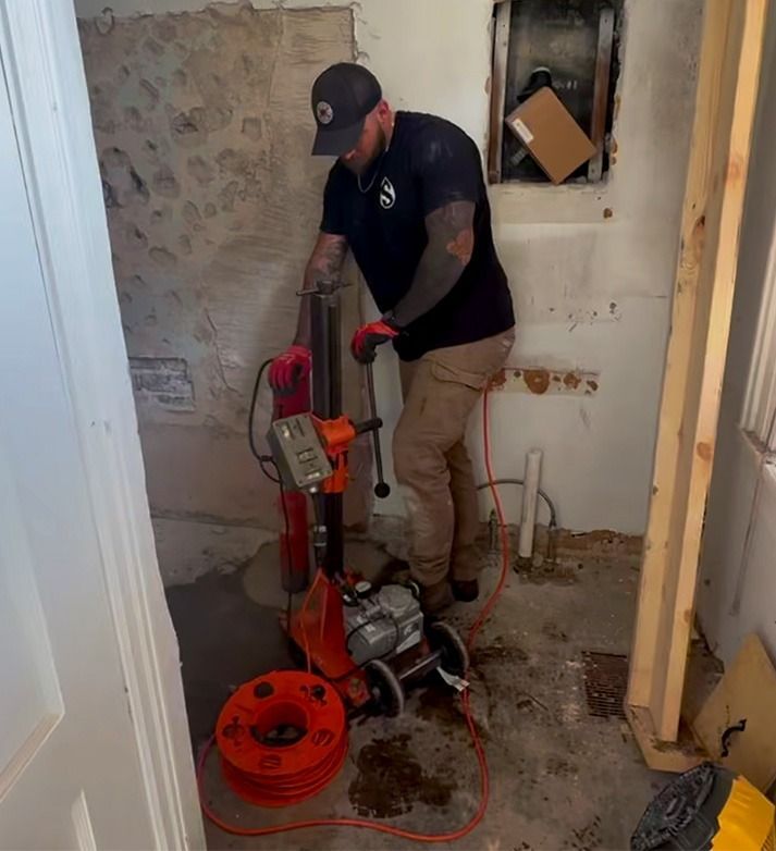 Worker using a red floor machine in a small room with damaged walls and debris on the floor