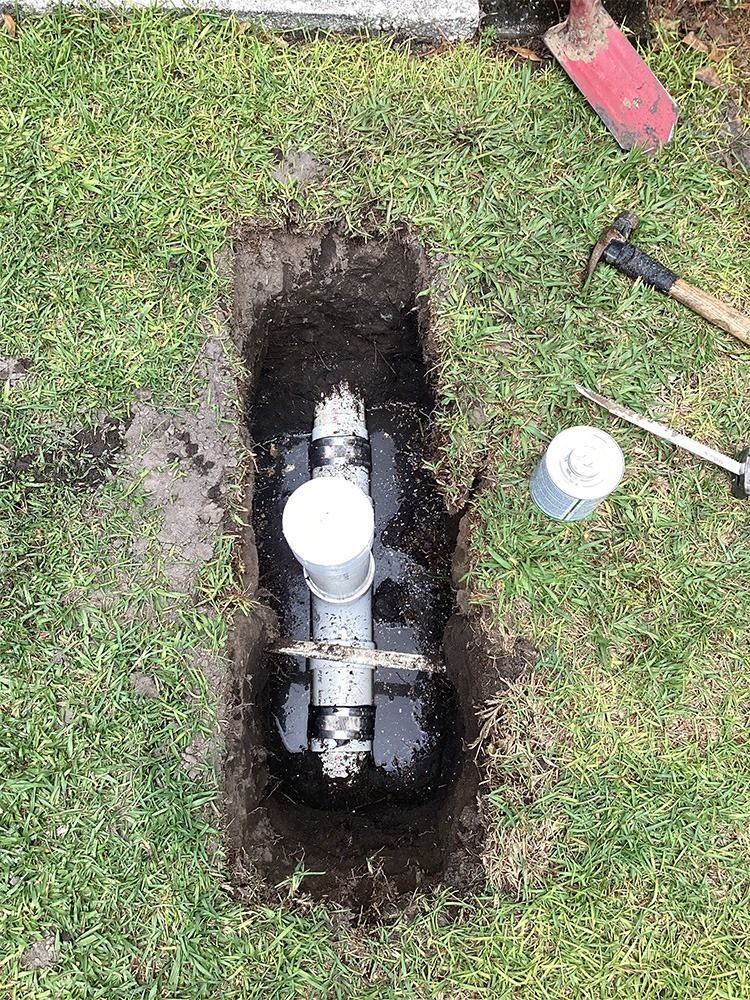 Sewer & Drain Services - Open water meter pit in grass with exposed pipe, tools, and a white cap nearby - Savannah, GA