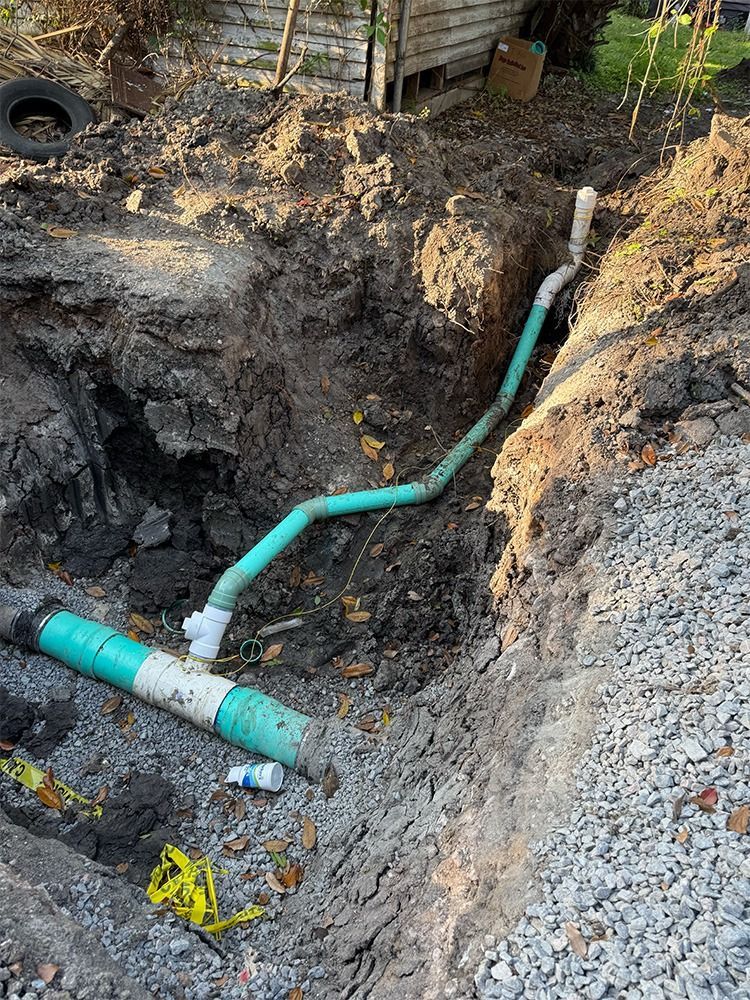 Water Line Repiping - Trench with exposed green pipe and white fittings in a dug-out dirt yard near a fence. - Savannah, GA