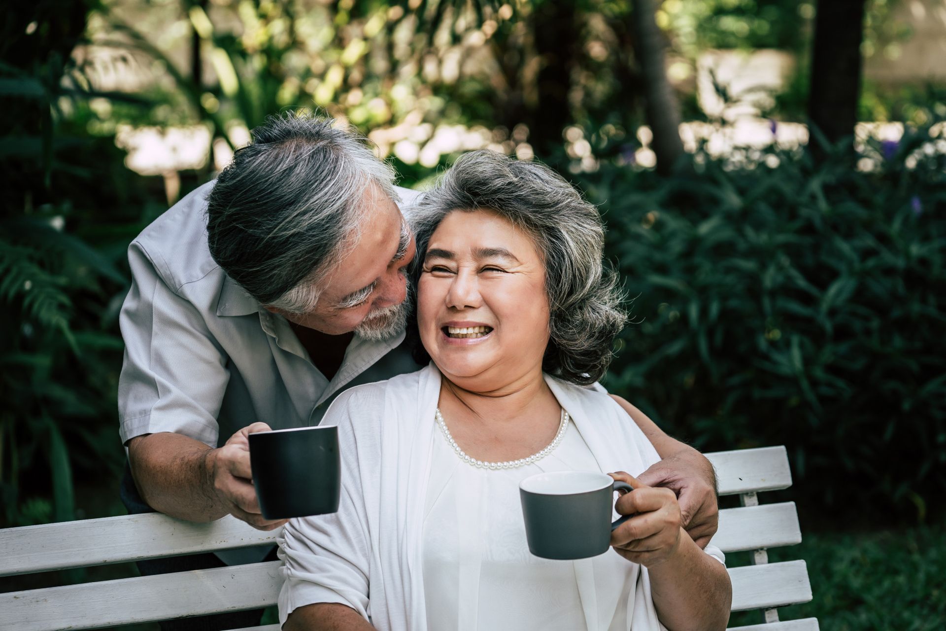 An elderly couple is sitting on a bench drinking coffee.