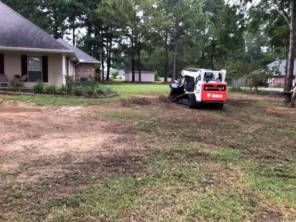 A bobcat is moving dirt in a yard in front of a house.