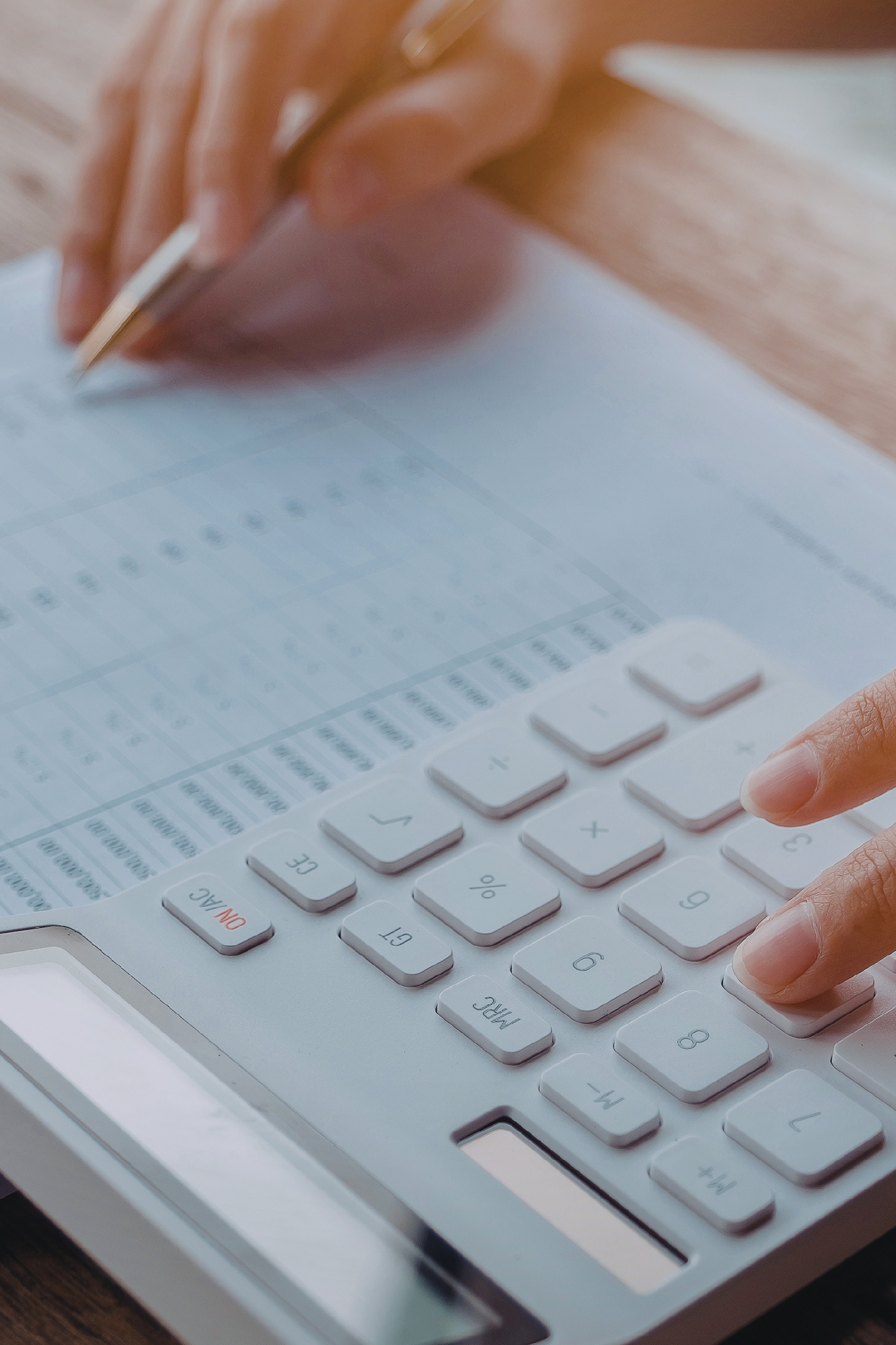 Hands using a calculator beside a ledger or spreadsheet.
