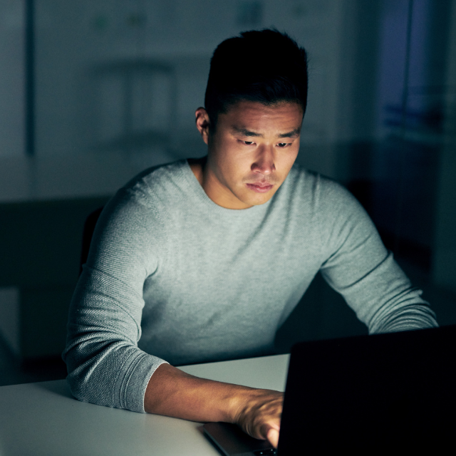 A man is sitting at a desk using a laptop computer at night.