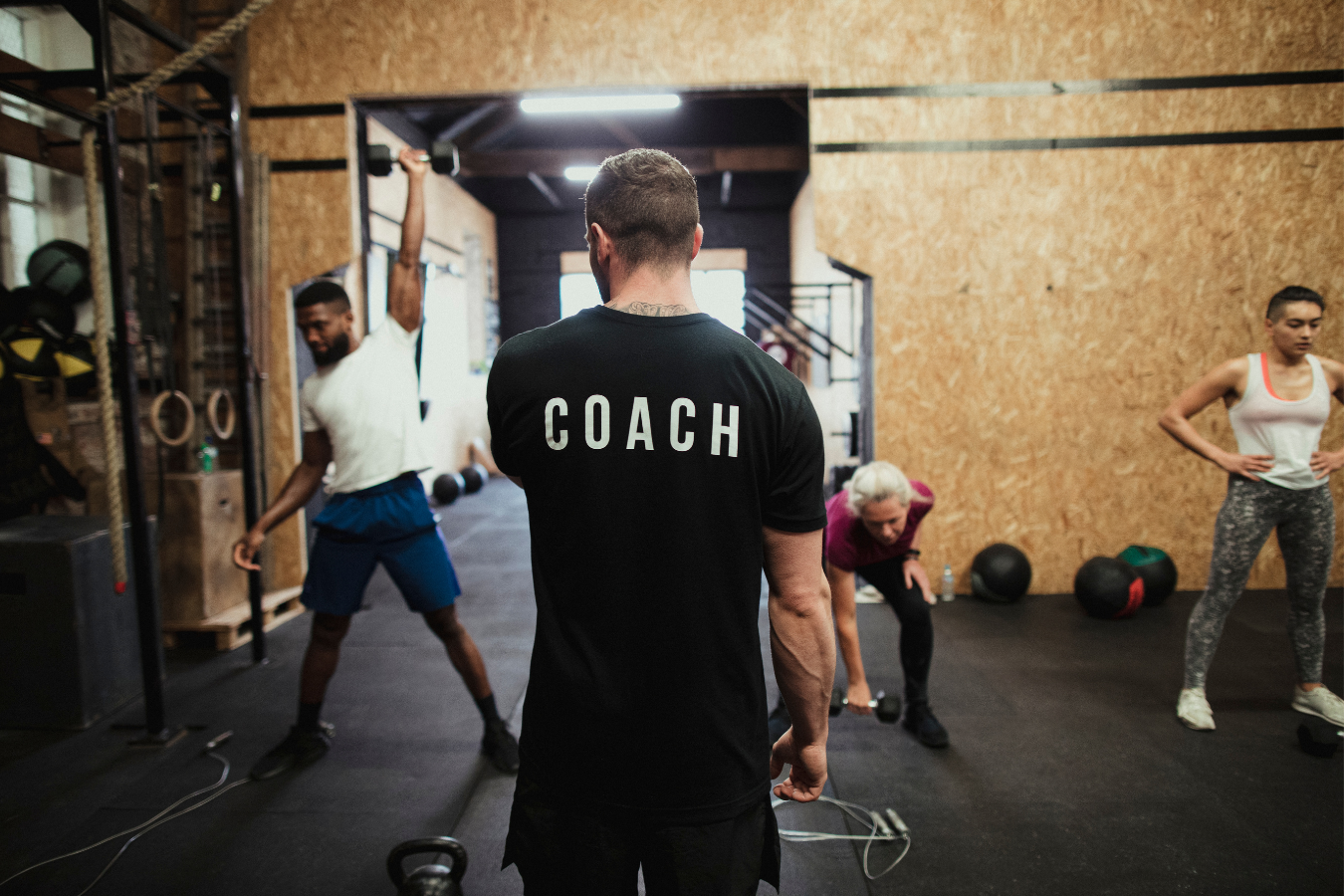 Fitness coach watches clients exercise in a gym.
