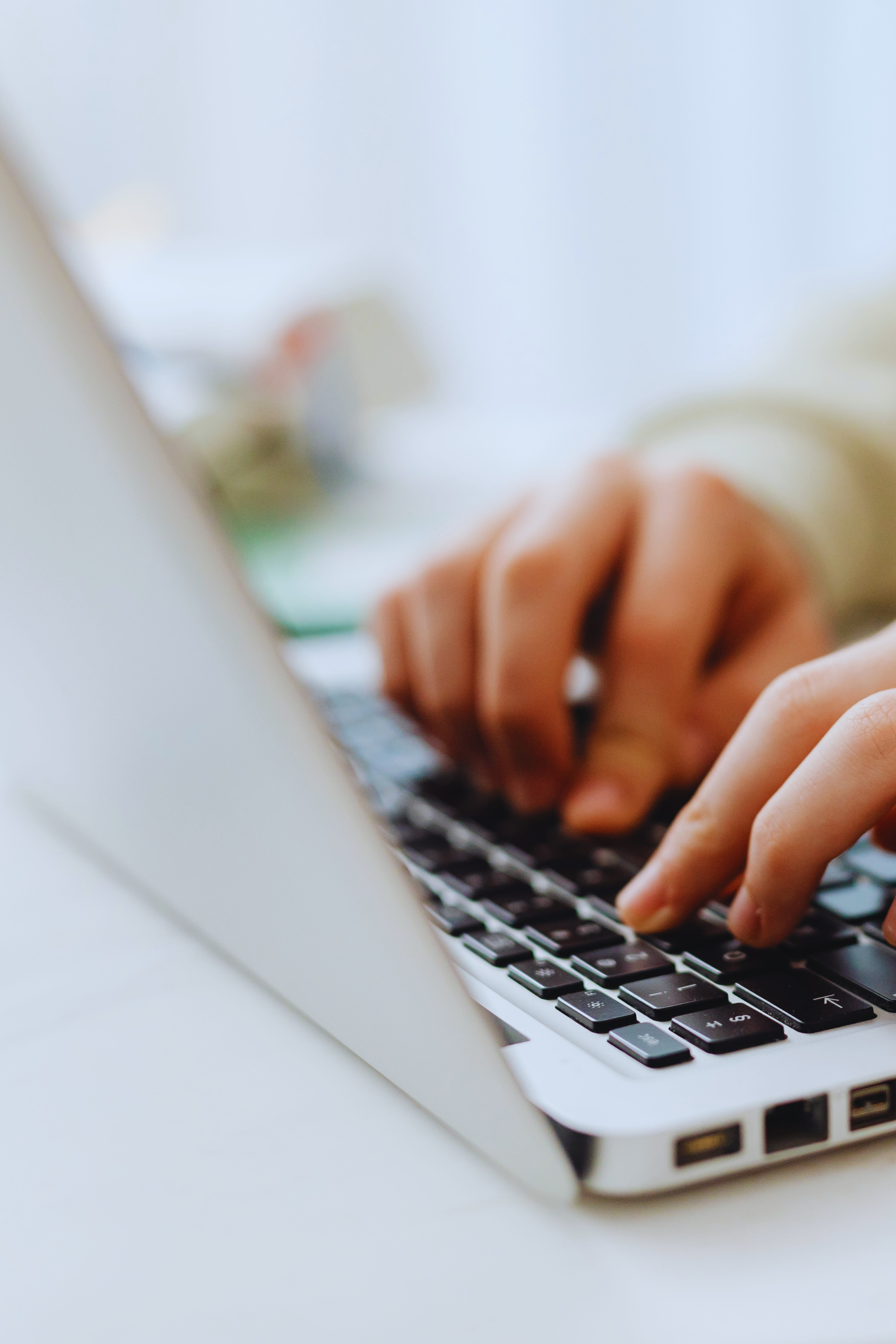 Hands typing on a laptop keyboard beside a white screen.